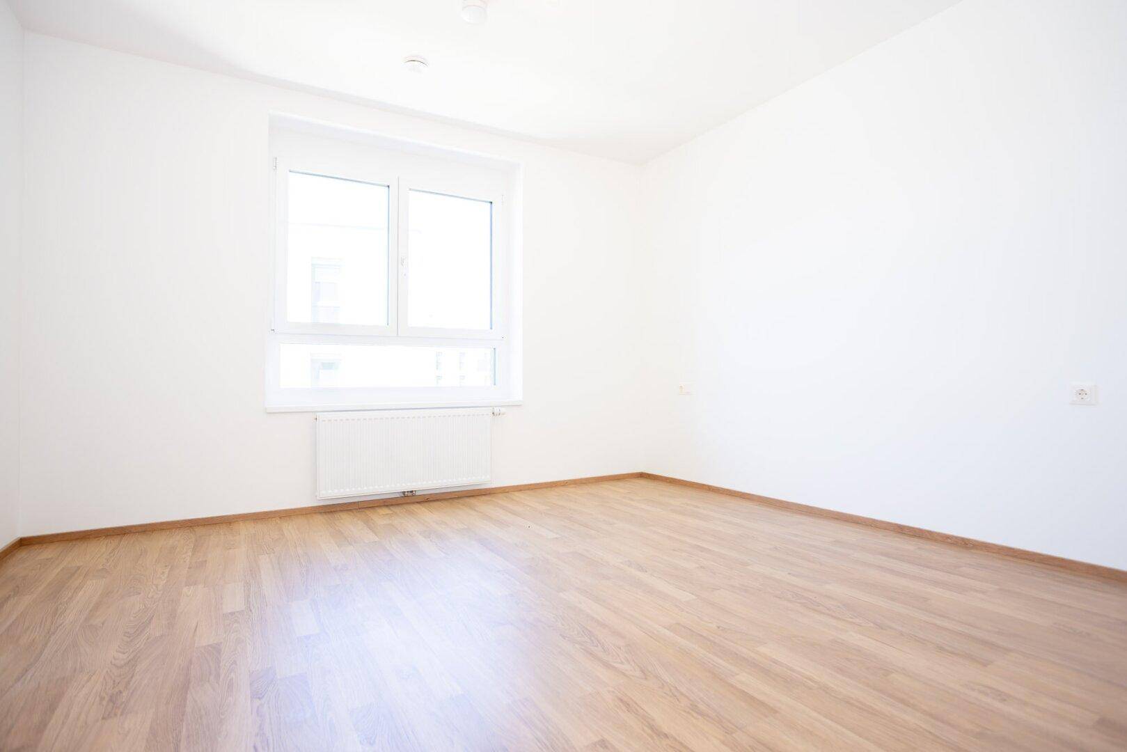 Helles Schlafzimmer mit Laminatboden, weißen Wänden und einem großen Fenster für viel Tageslicht.