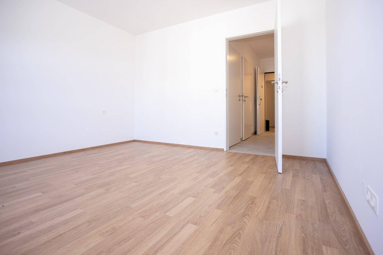 Leeres Schlafzimmer mit Laminatboden und weiß gestrichenen Wänden, bereit zur individuellen Gestaltung.