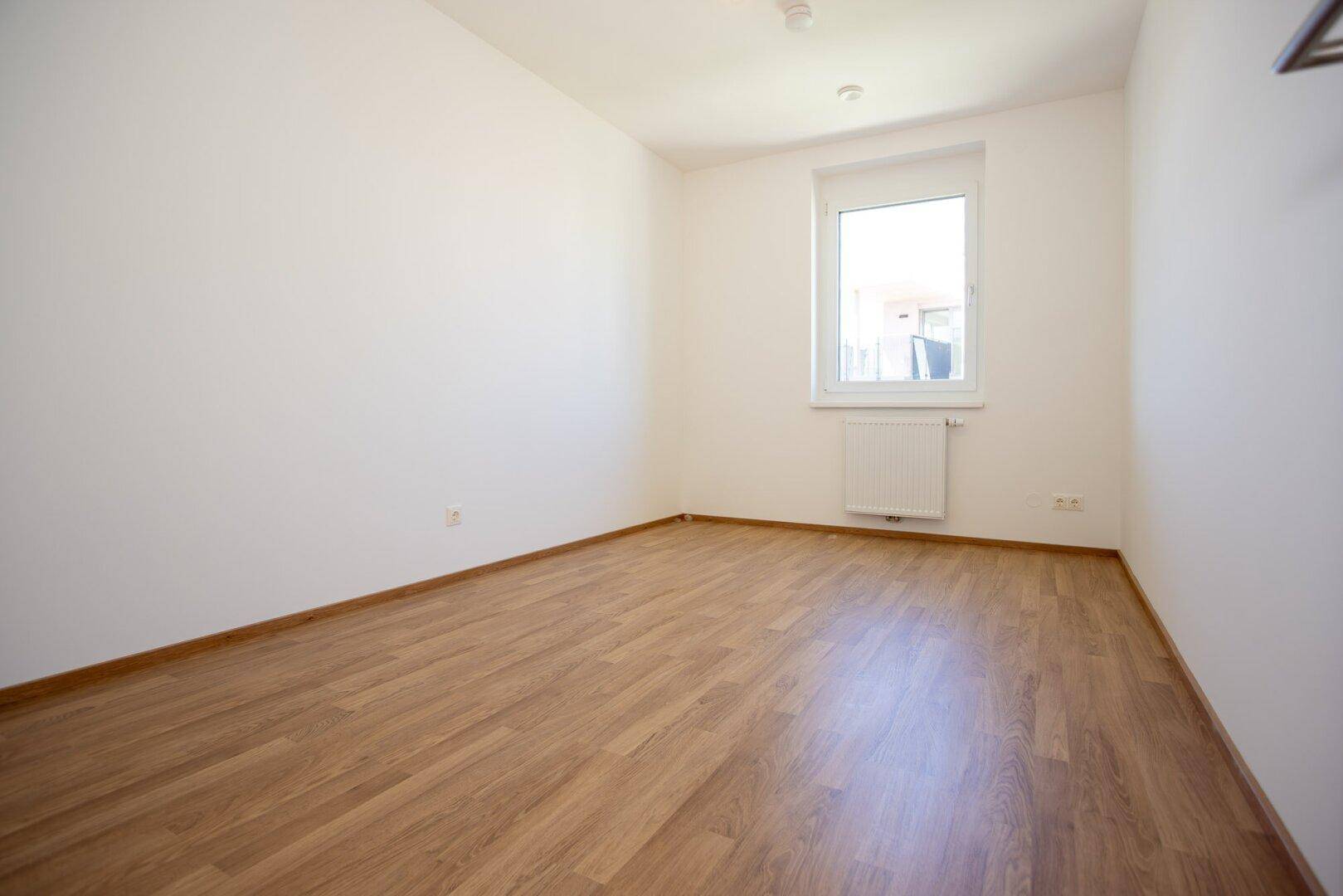 Helles Zimmer mit Laminatboden und einem Fenster, ideal als Kinderzimmer oder Büro nutzbar.
