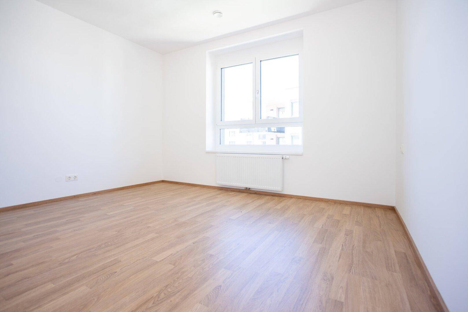 Geräumiges Schlafzimmer mit hellem Laminatboden und einem Fenster, das den Raum gut belichtet.