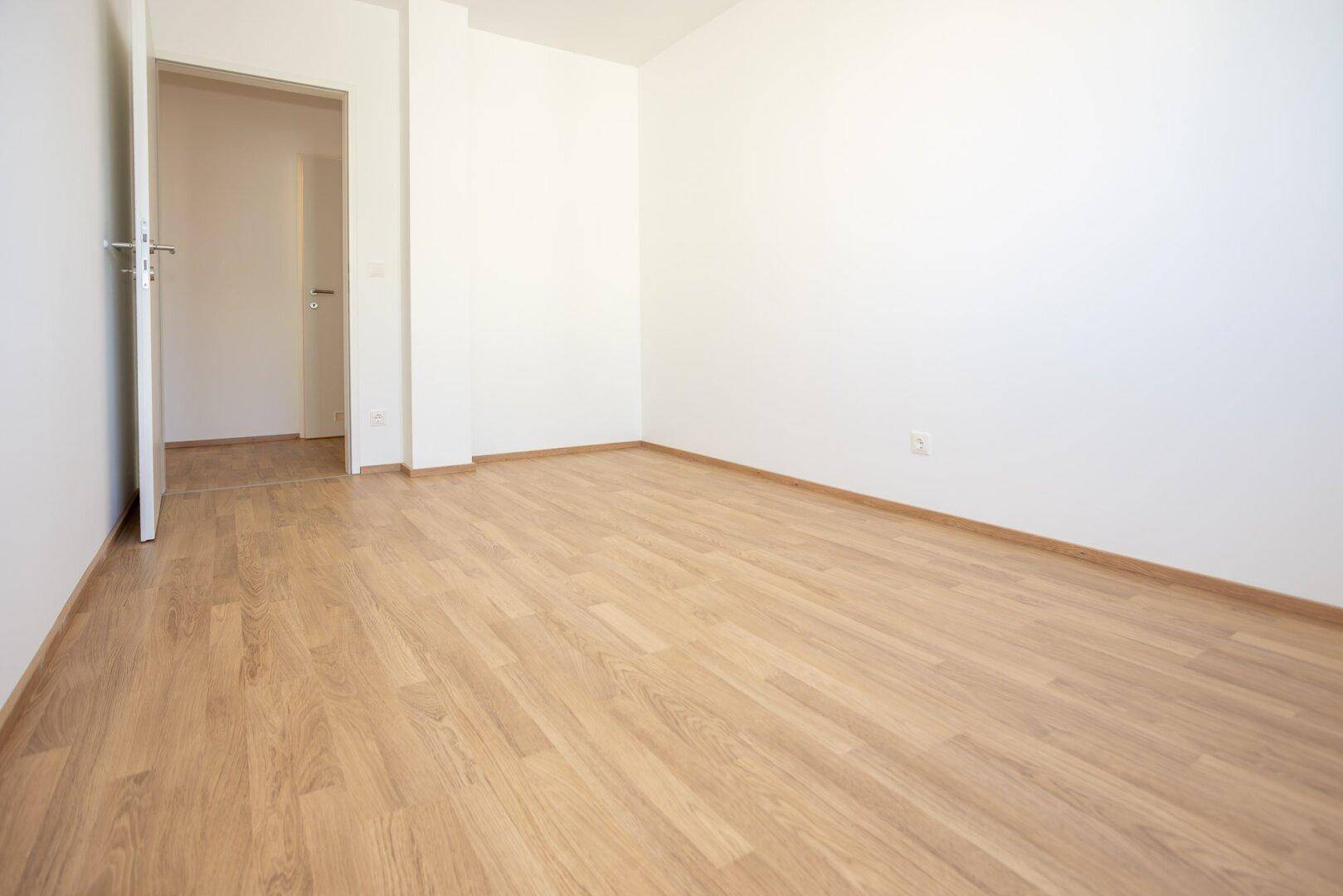 Geräumiges Zimmer mit Laminatboden und weißen Wänden, bietet viel Platz für individuelle Einrichtung.