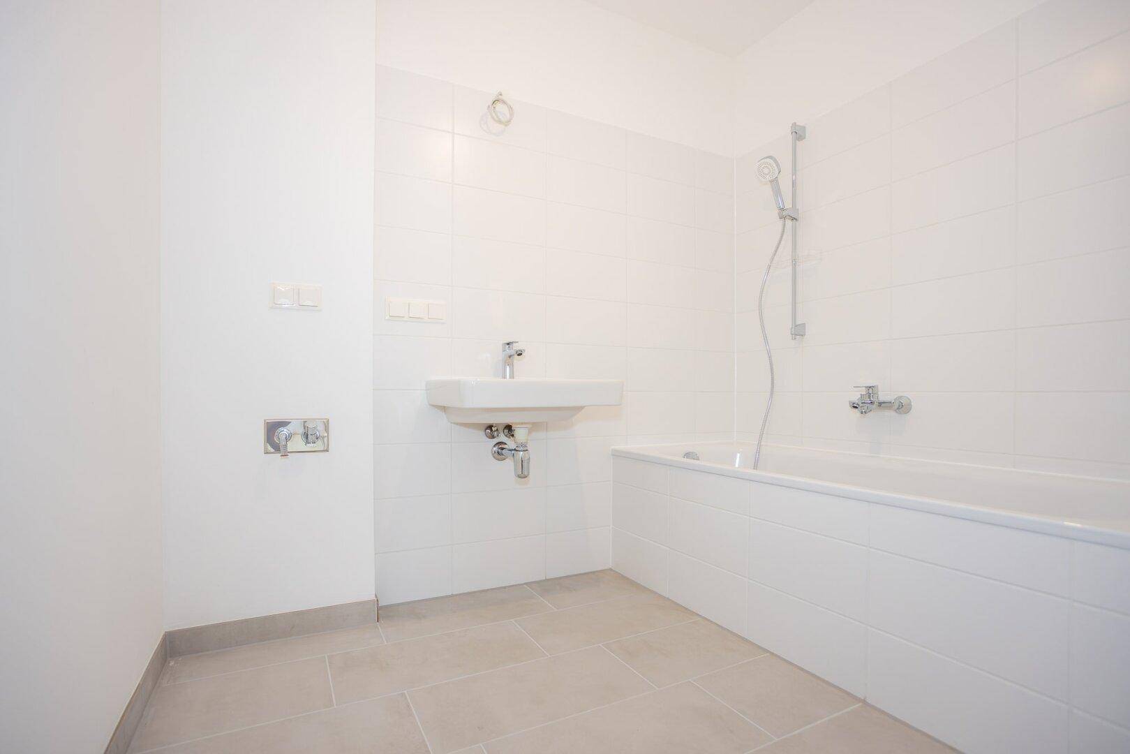 Modernes Badezimmer mit Badewanne, Dusche und Waschbecken in hellen Fliesen.