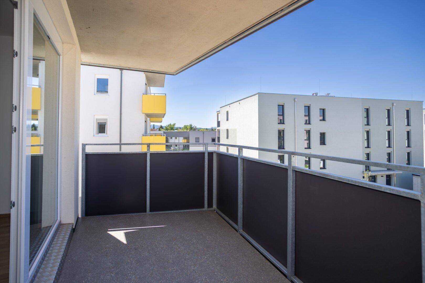 Heller Balkon mit moderner Brüstung und Ausblick auf die Wohnanlage.