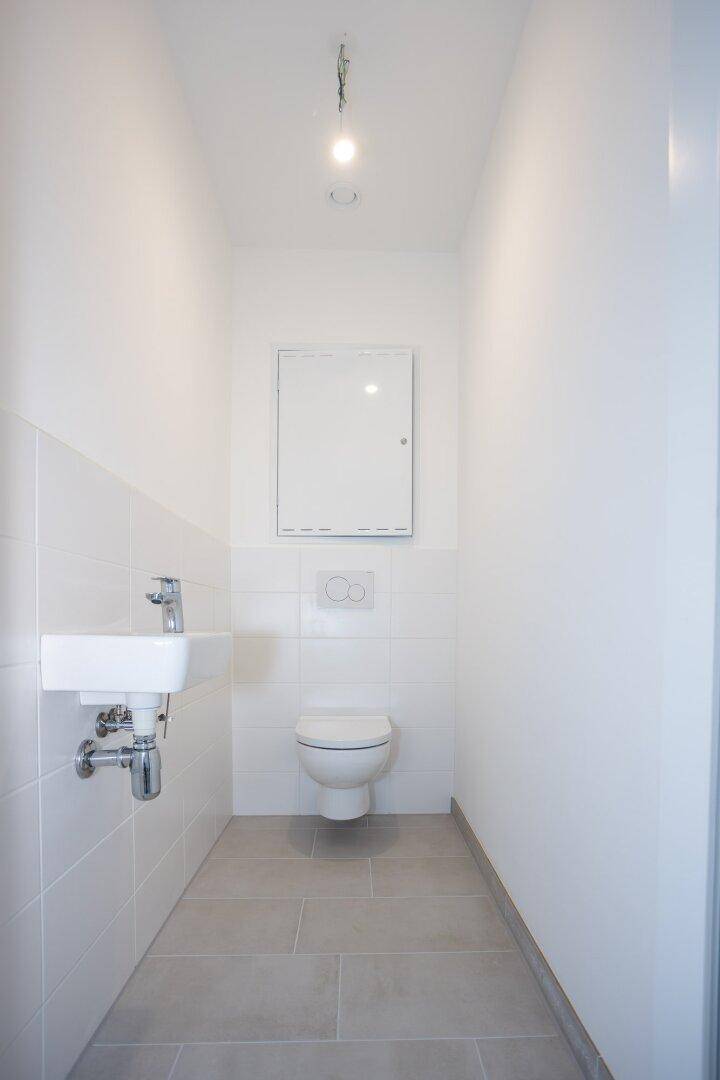 Separates Gäste-WC mit wandhängender Toilette und kleinem Handwaschbecken.