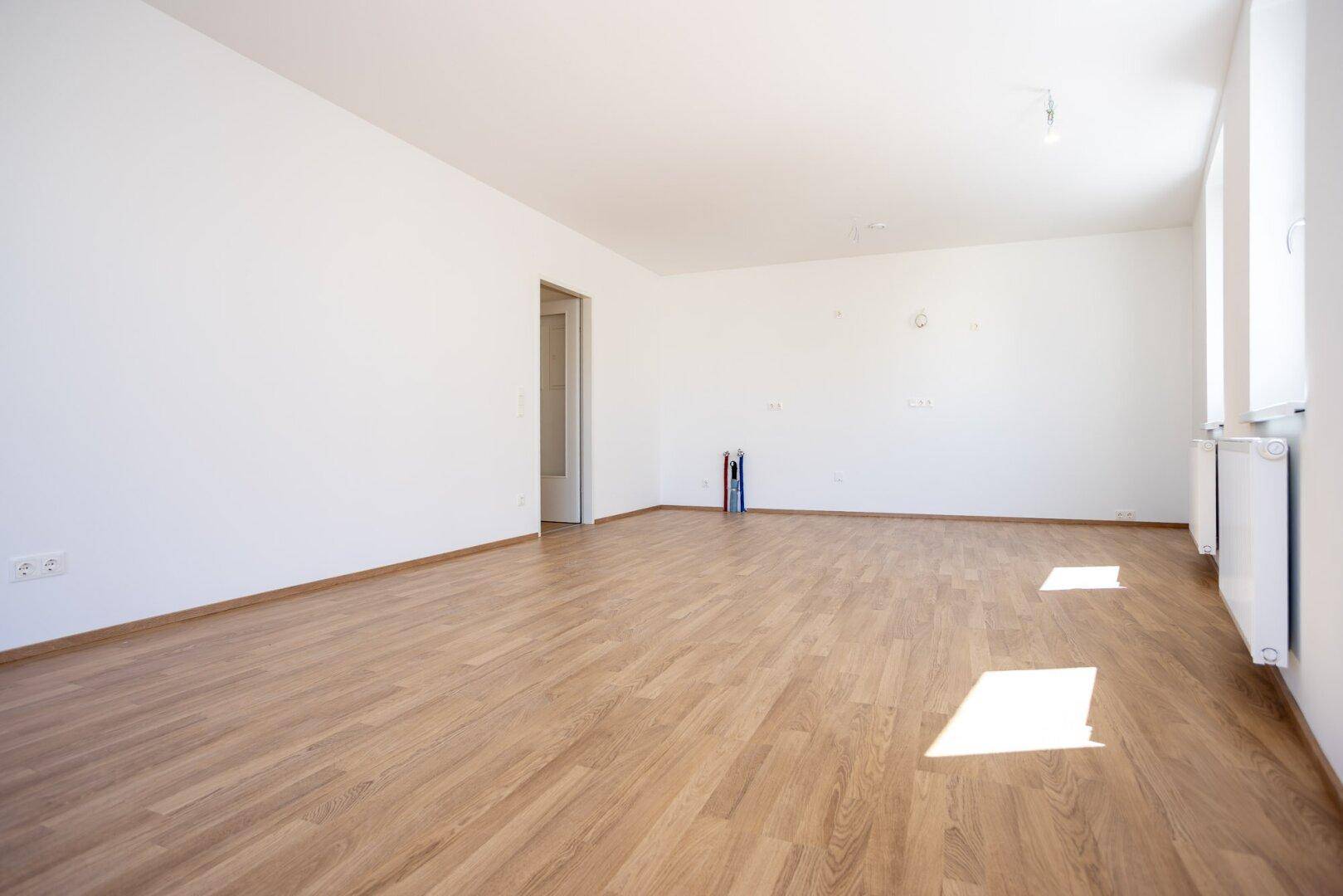 Leerer Küchenbereich mit Anschlüssen für eine Einbauküche und hellem Laminatboden.