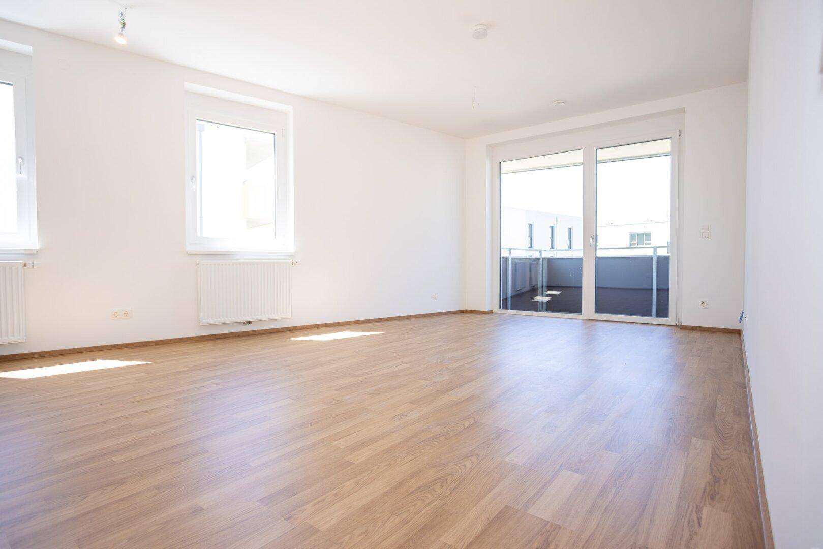 Helles Wohnzimmer mit Laminatboden und Zugang zu einem sonnigen Balkon.