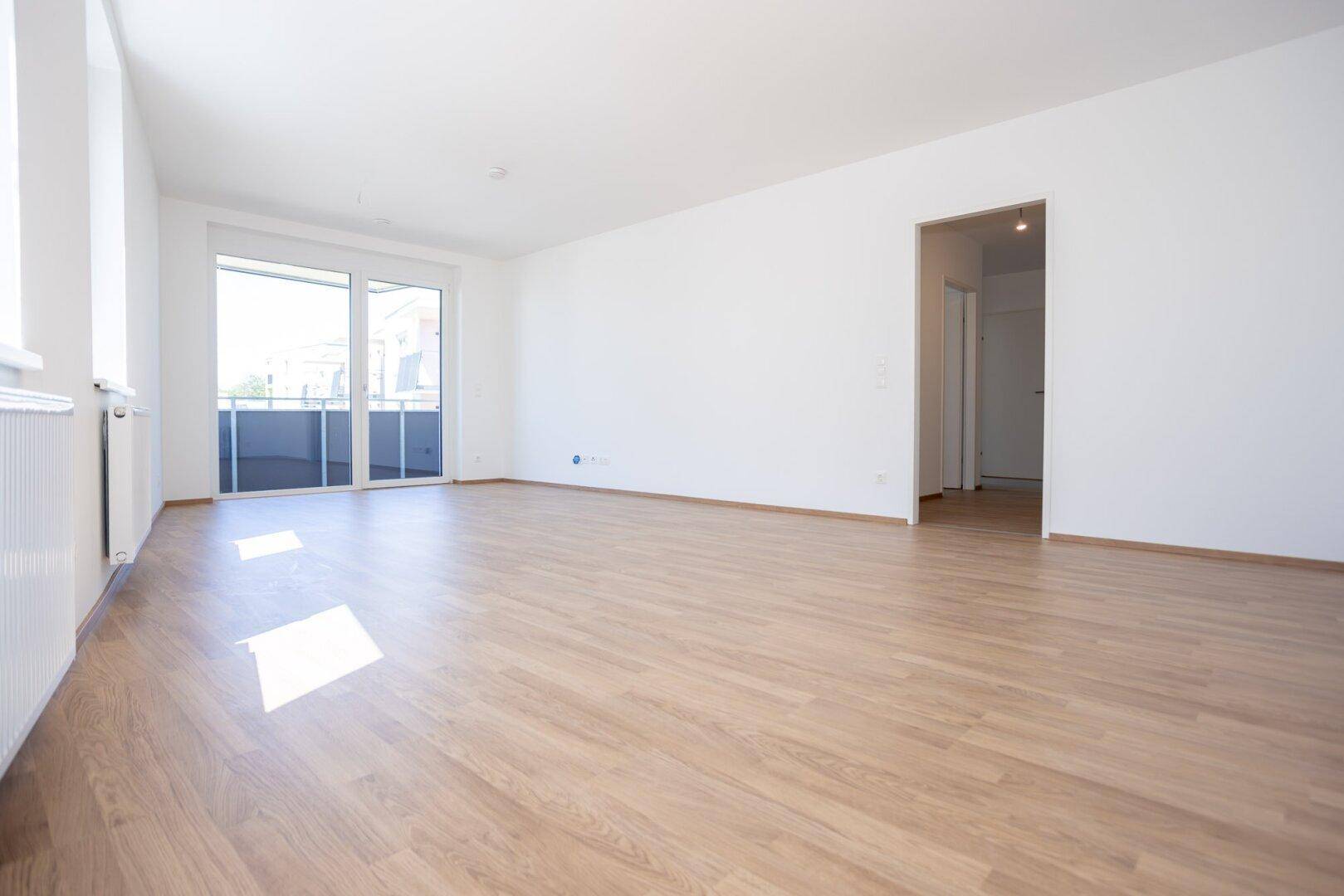 Geräumiges Wohnzimmer mit hellem Laminatboden und direktem Zugang zum Außenbereich.