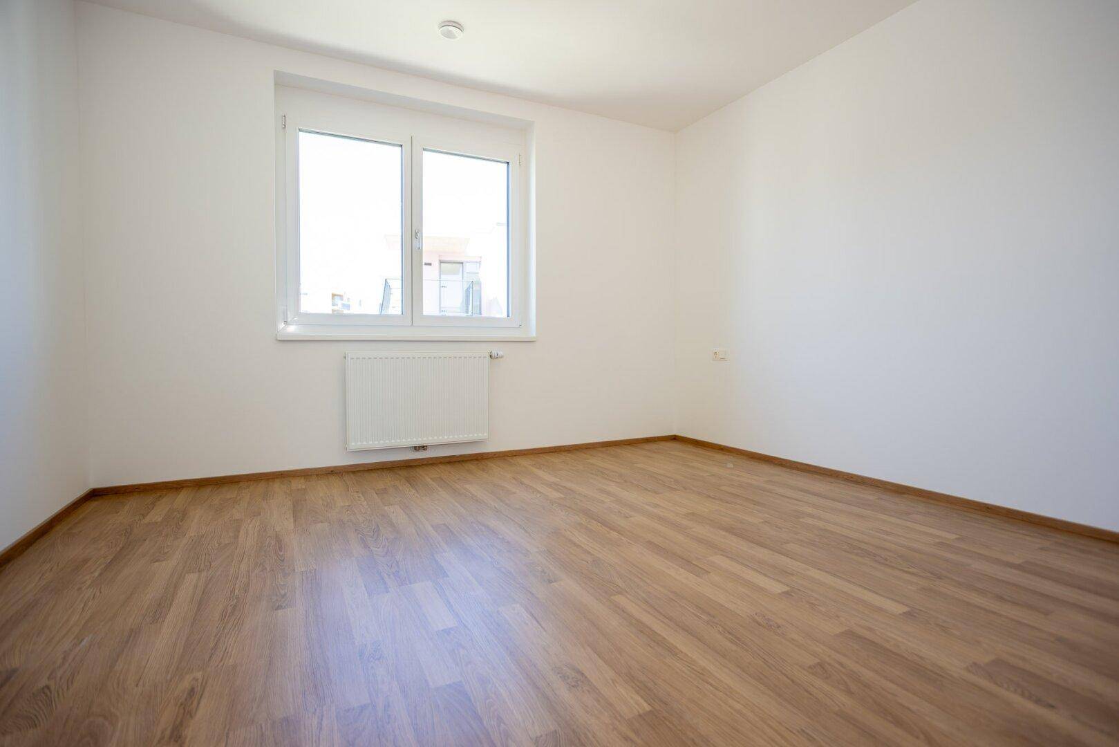 Ruhiges Schlafzimmer mit hellem Laminatboden und einem großen Fenster.