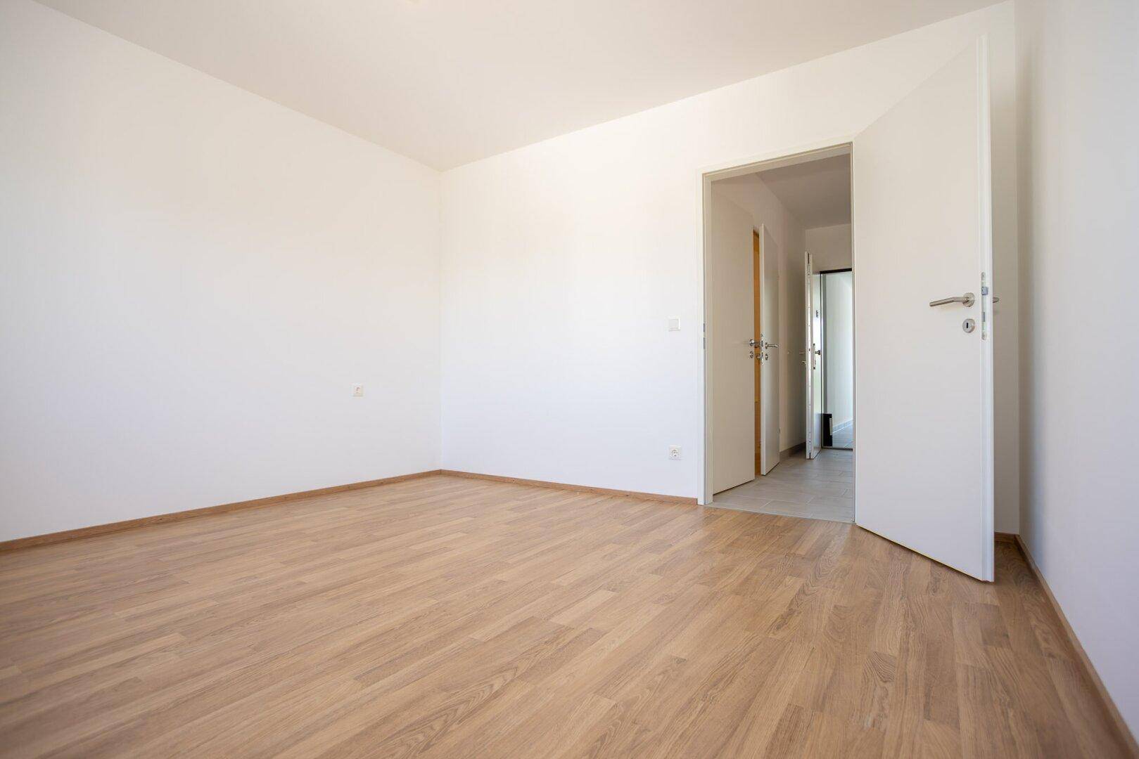 Geräumiges Zimmer mit Laminatboden und Zugang zu einem gefliesten Flur.