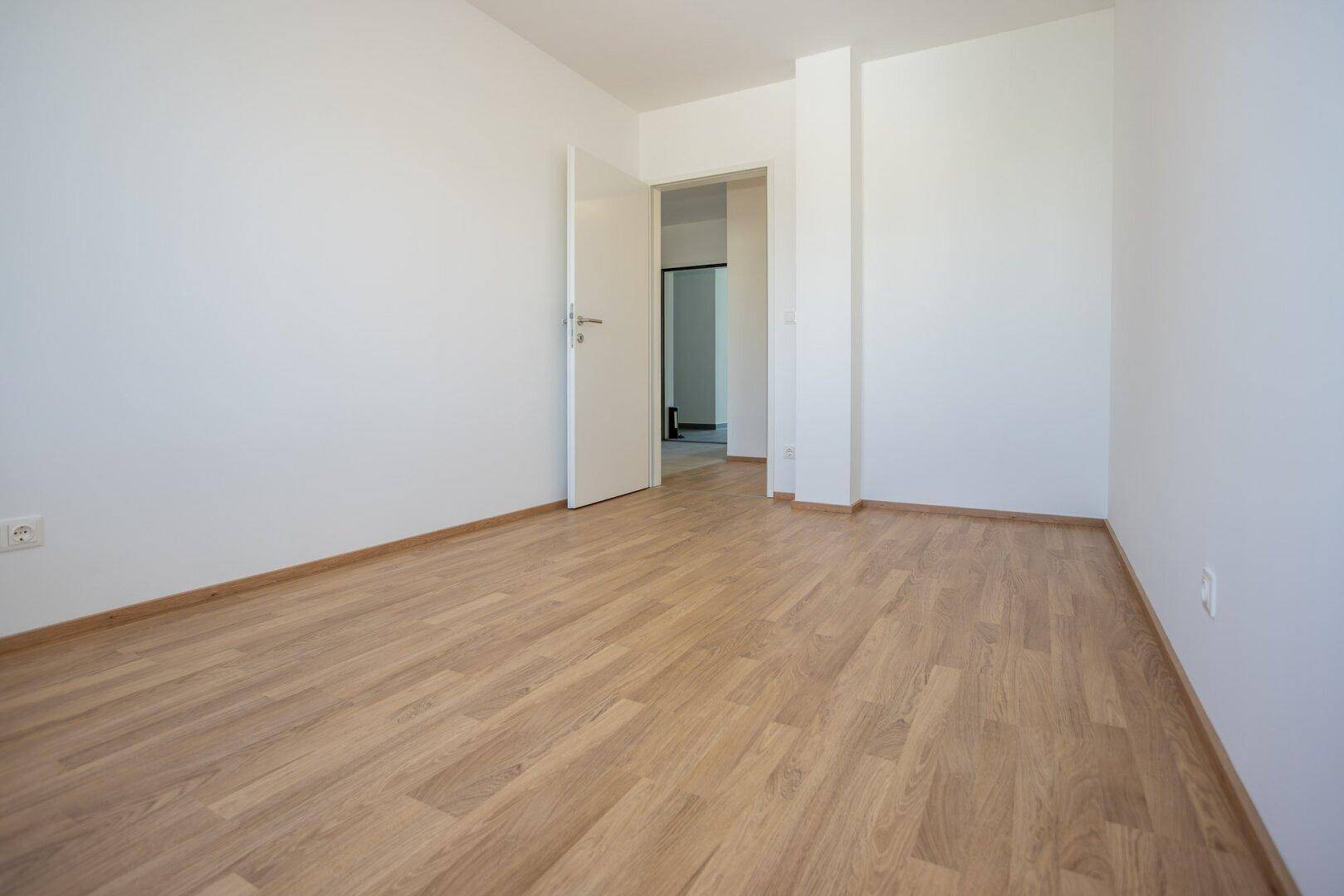 Geräumiges Zimmer mit Laminatboden und Zugang zu weiteren Räumen.