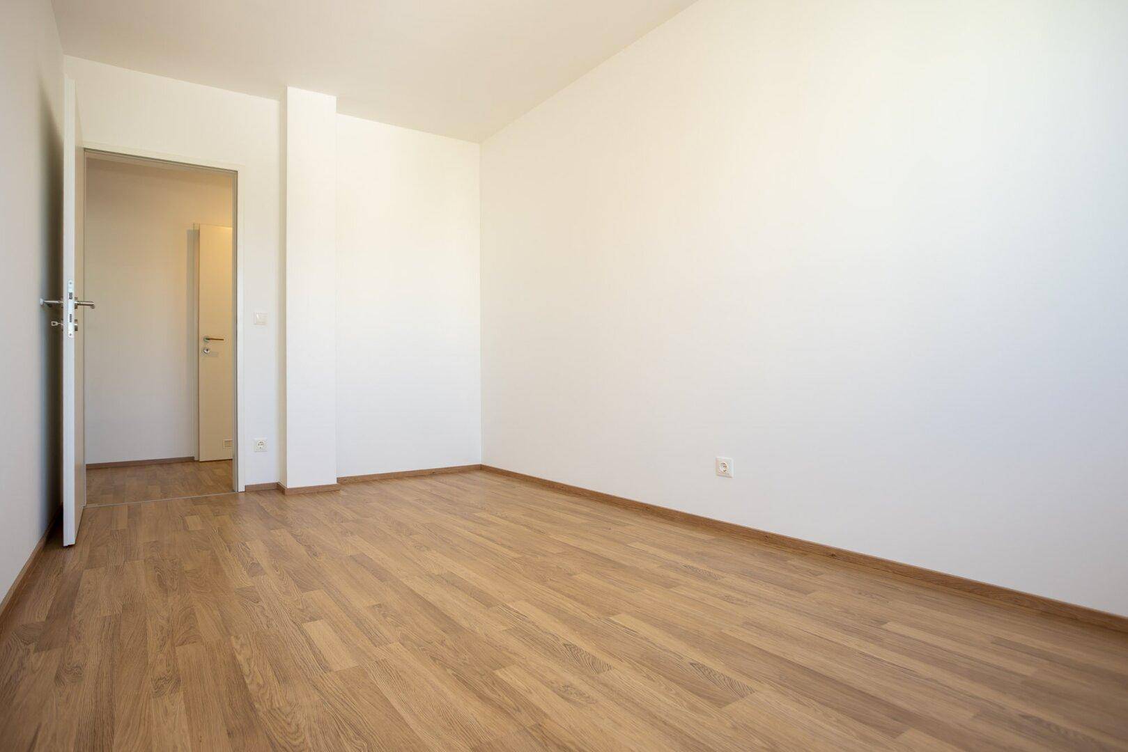 Heller Raum mit Laminatboden und weiß gestrichenen Wänden, bereit zum Einzug.