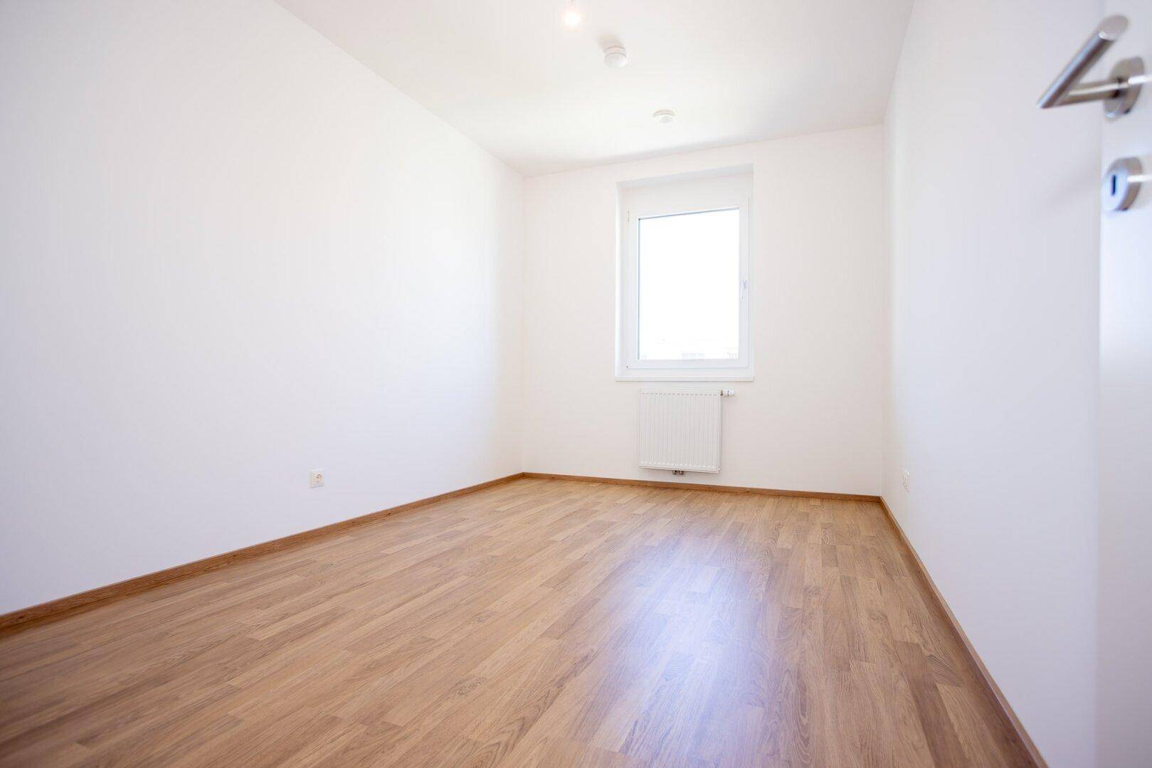 Helles Zimmer mit Laminatboden und einem Fenster, ideal als Kinder- oder Arbeitszimmer.