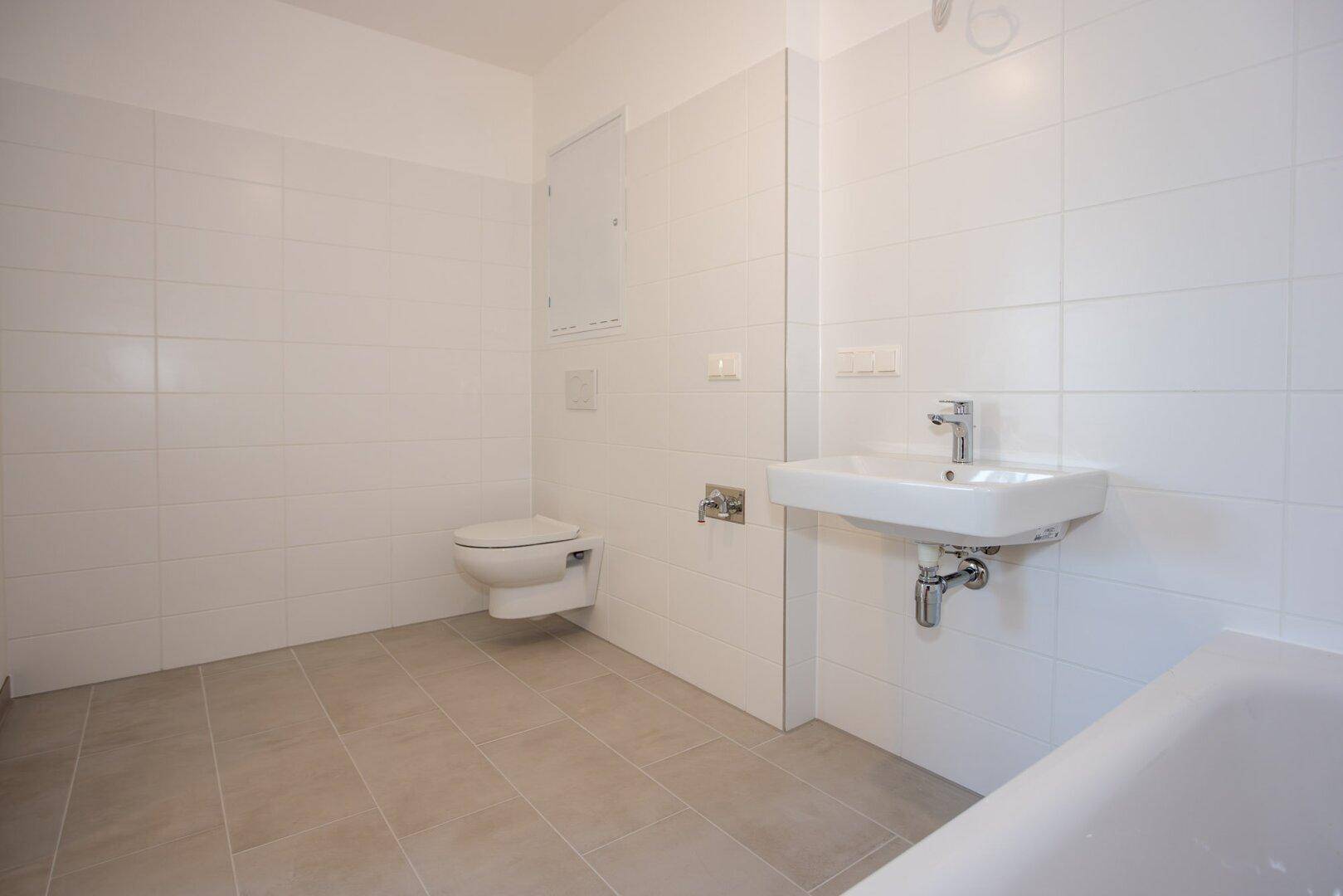 Helles Badezimmer mit zeitgemäßen Armaturen, Badewanne und wandhängendem WC.