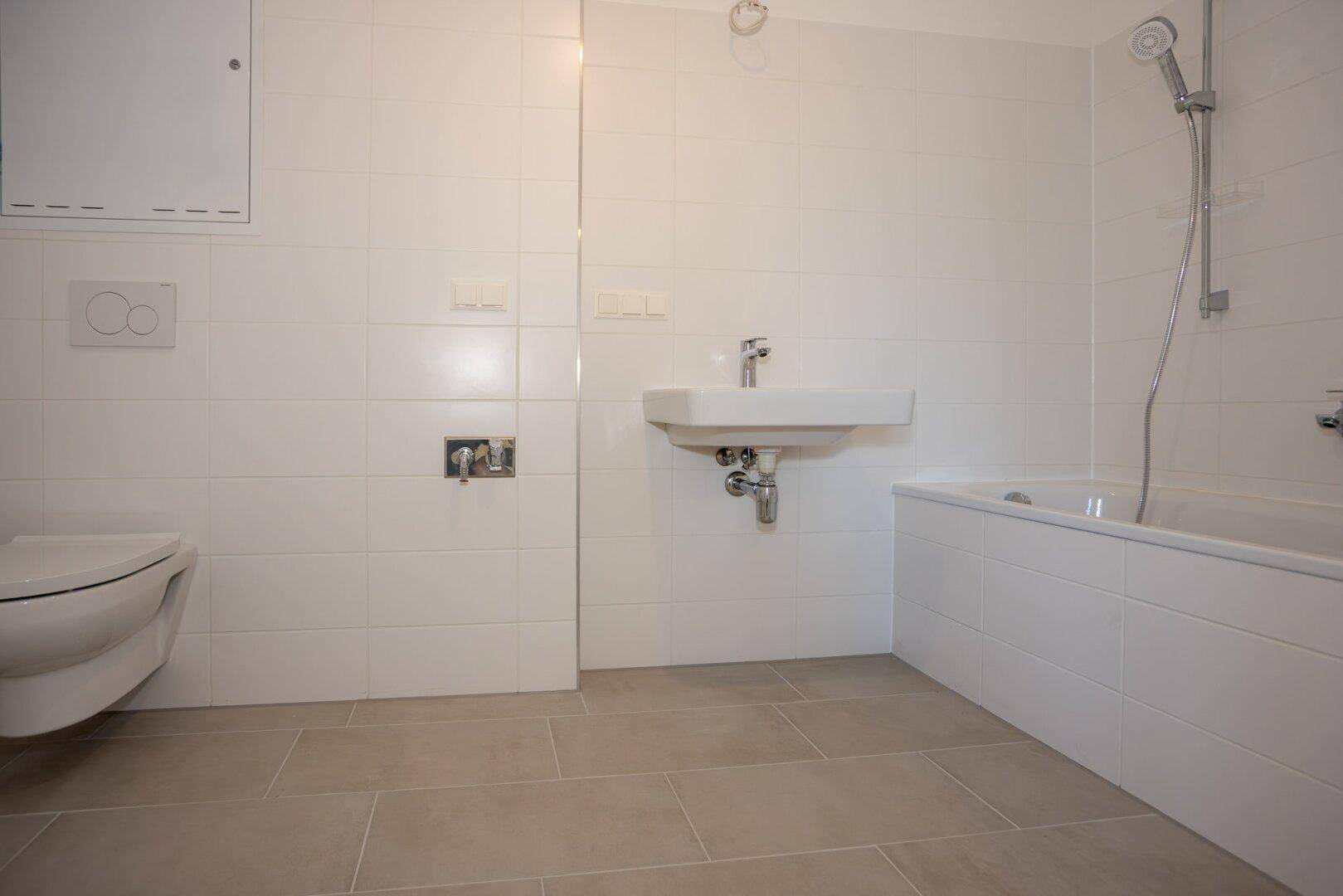 Modernes Badezimmer mit weißen Fliesen, Badewanne, WC und Waschbecken.