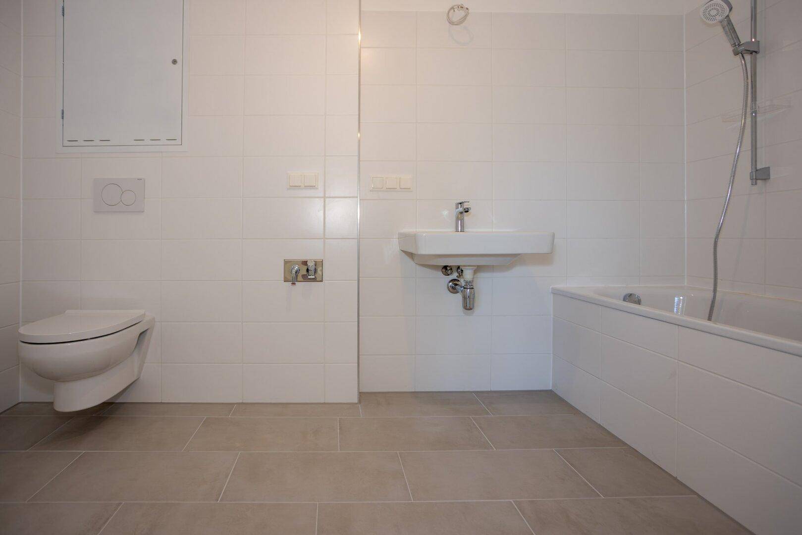 Funktionales Badezimmer mit weißen Wandfliesen und hellgrauem Boden, ausgestattet mit Badewanne.