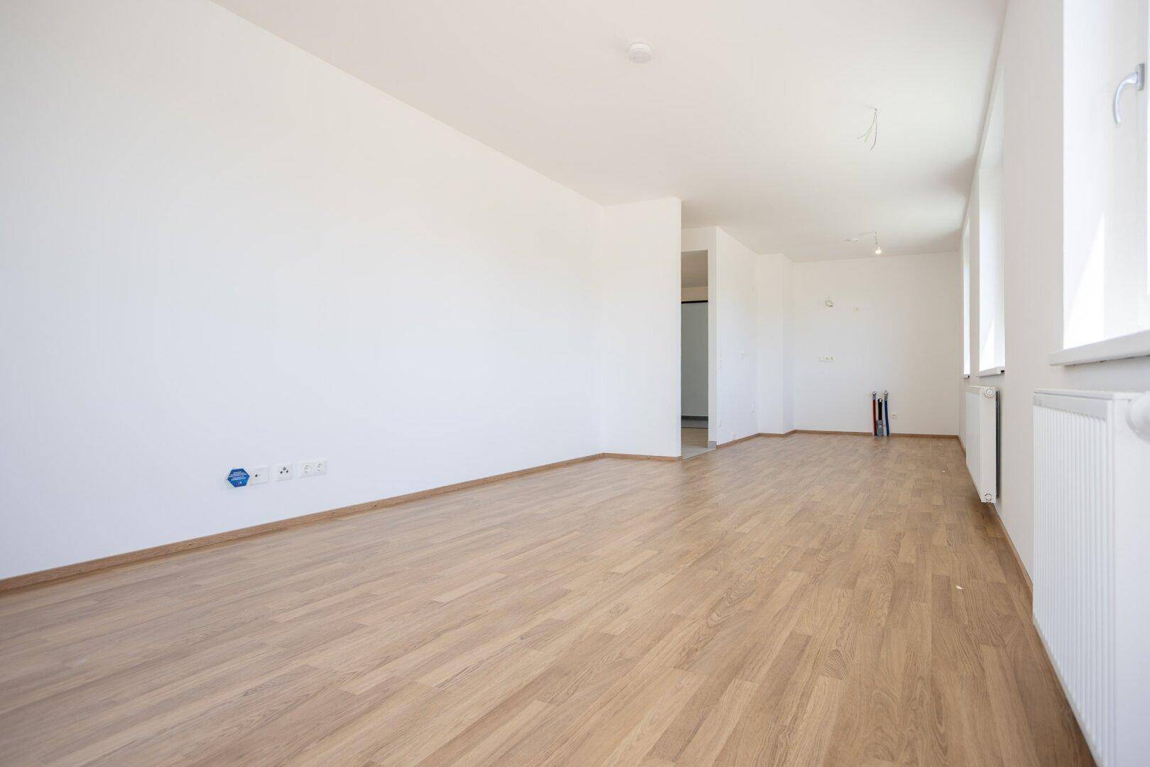Geräumiger, unmöblierter Raum mit hellem Holzboden und frisch gestrichenen weißen Wänden.