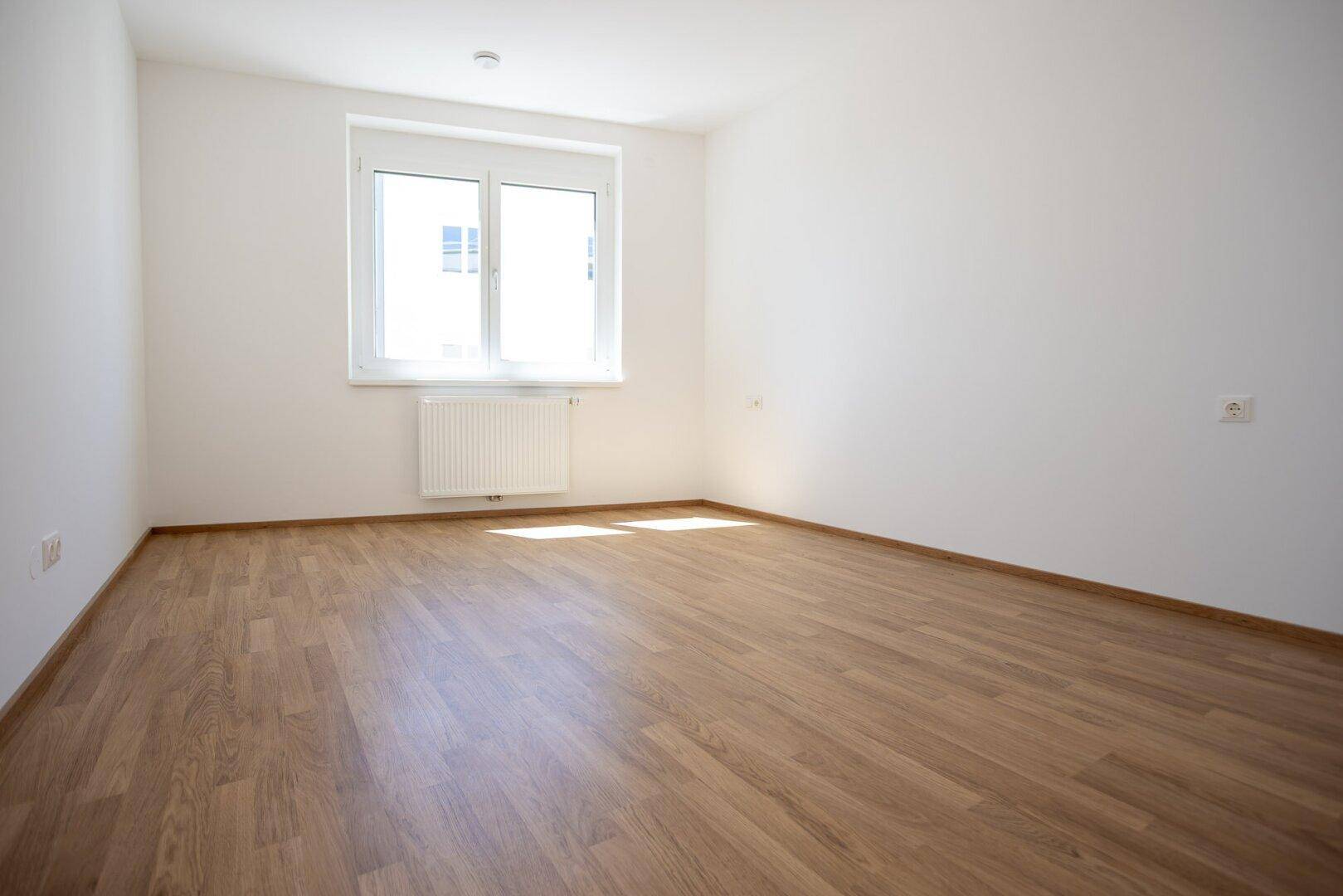 Ruhiges Schlafzimmer mit hellem Holzboden und einem großen Fenster für natürliches Licht.