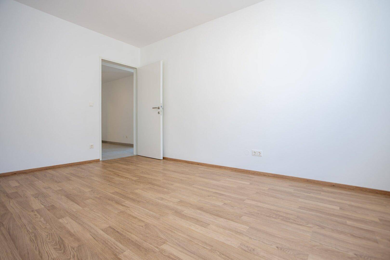 Heller Raum mit Holzboden und offener Tür, der als Schlaf- oder Arbeitszimmer dienen könnte.