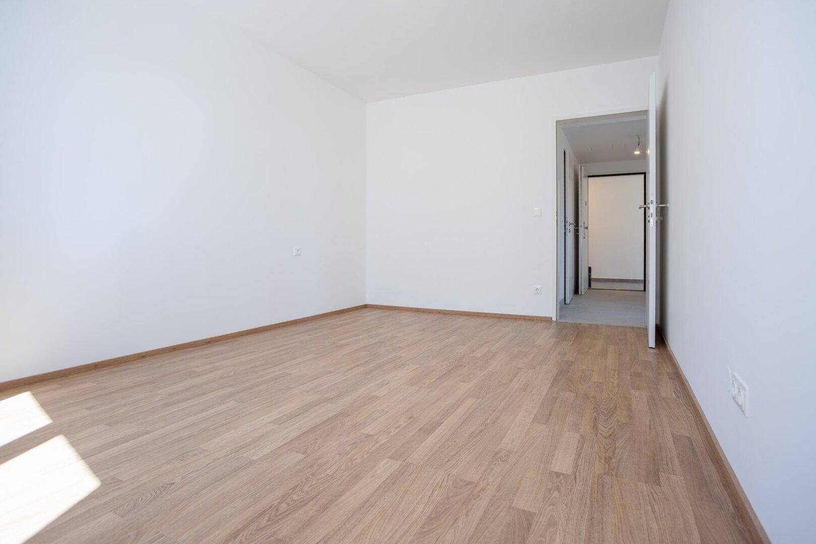 Unmöblierter Raum mit Holzboden und Zugang zu einem Flur, ideal für individuelle Gestaltung.