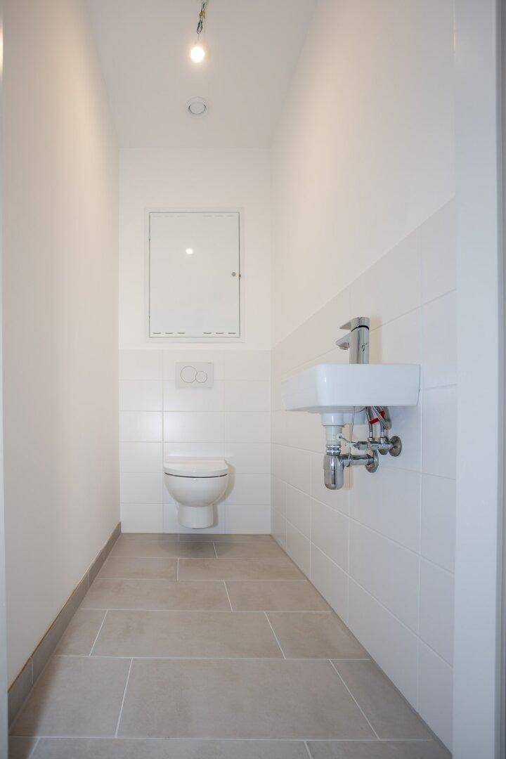 Modernes Gäste-WC mit wandhängender Toilette und kleinem Waschbecken, hell gefliest in Weiß und Grau.