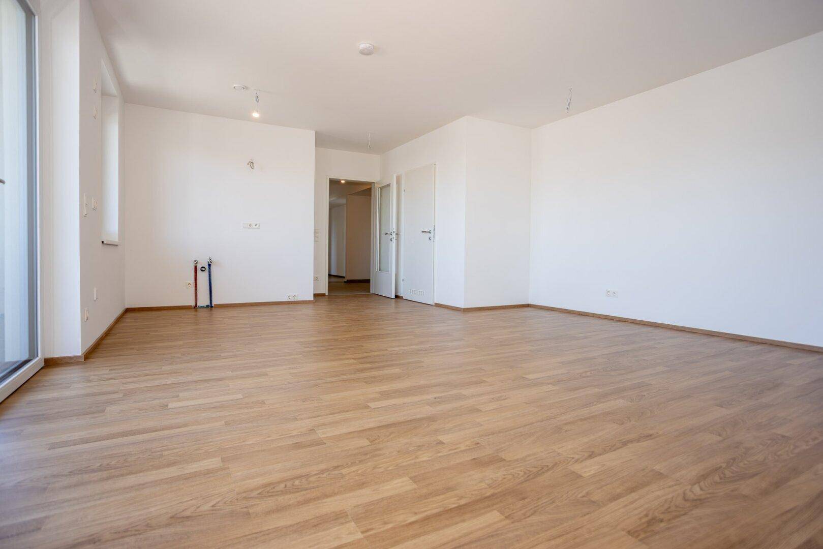 Geräumiger, unmöblierter Wohnbereich mit hellem Laminatboden und weißen Wänden, bereit zum Einzug.