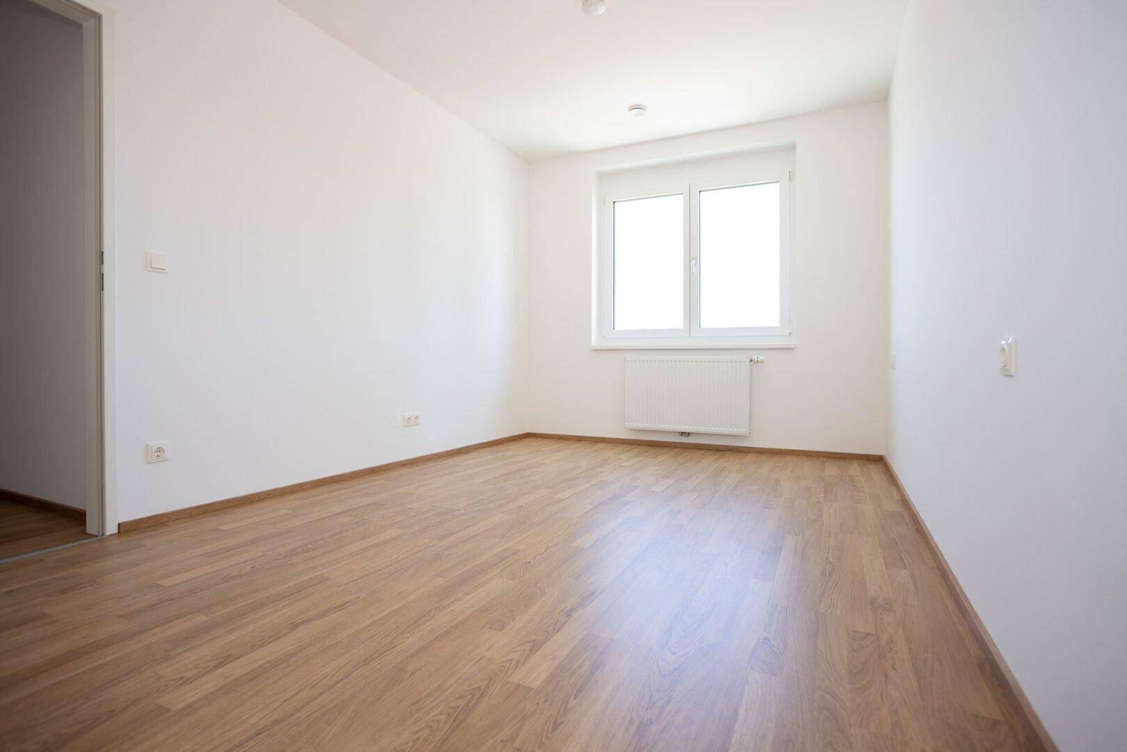 Geräumiges Schlafzimmer mit hellem Laminatboden und weißen Wänden, bereit zur individuellen Einrichtung.