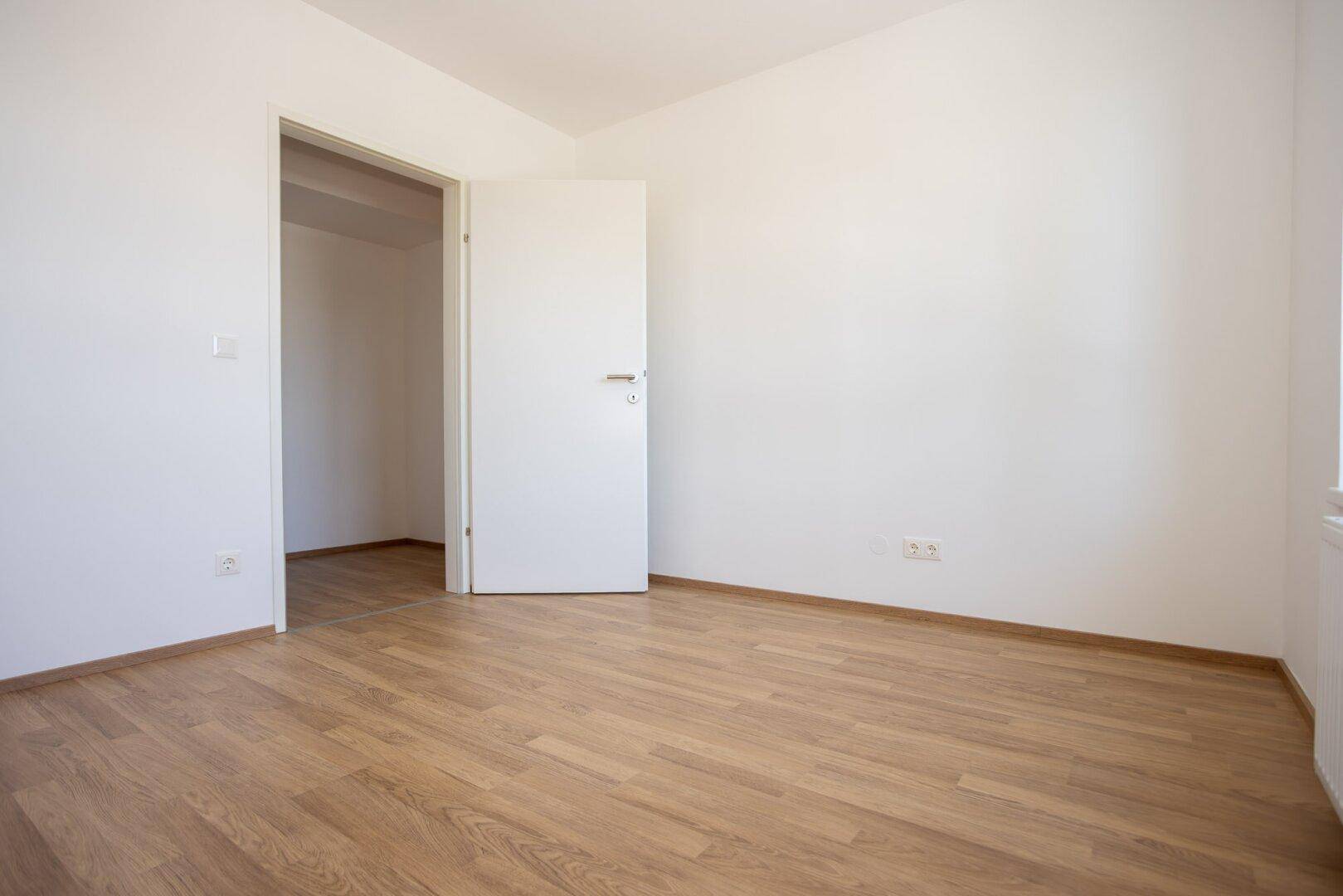 Helles Schlafzimmer mit Laminatboden und offener Tür, das vielseitige Nutzungsmöglichkeiten bietet.