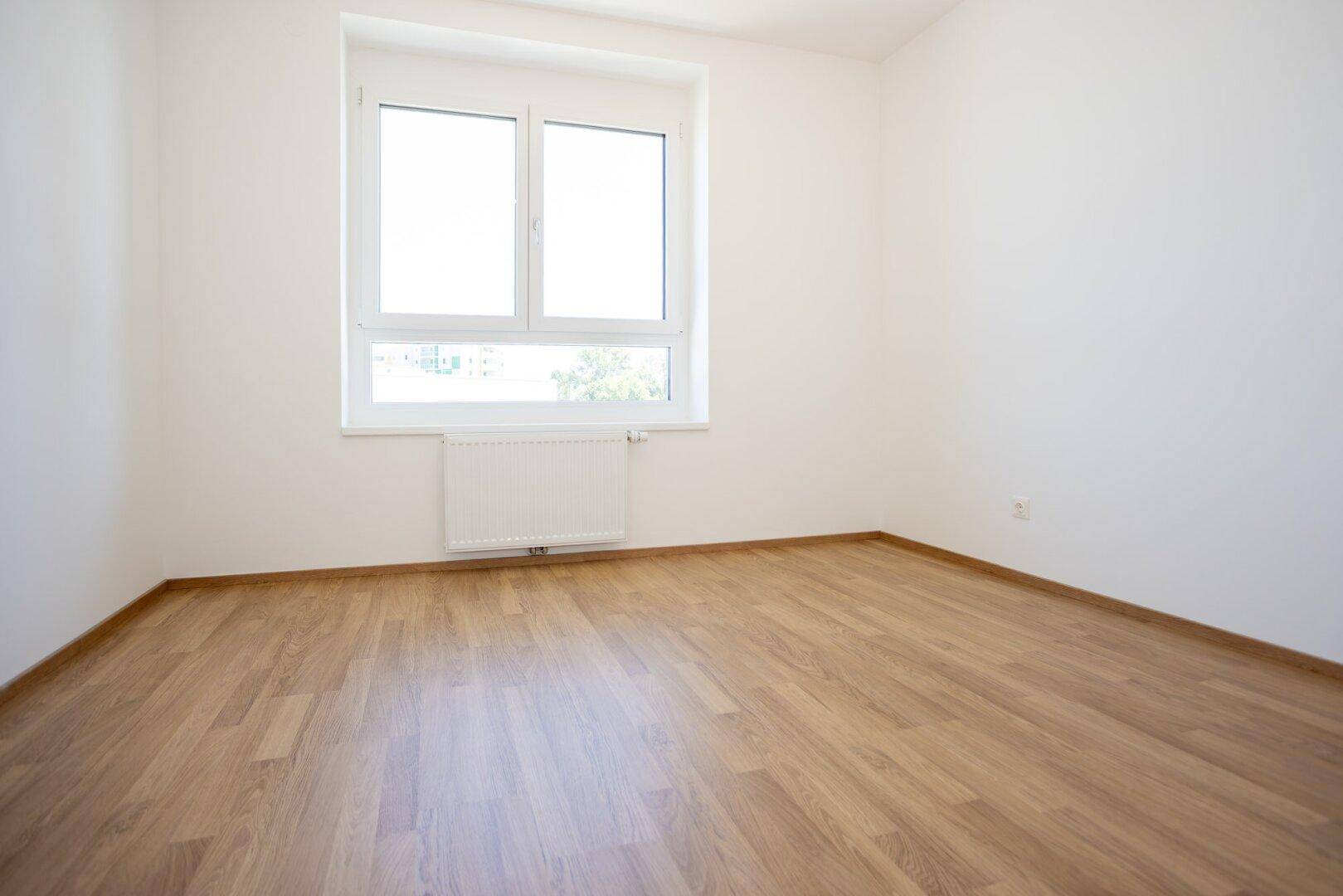 Freundliches Schlafzimmer mit Laminatboden und einem großen Fenster, das für eine angenehme Atmosphäre sorgt.