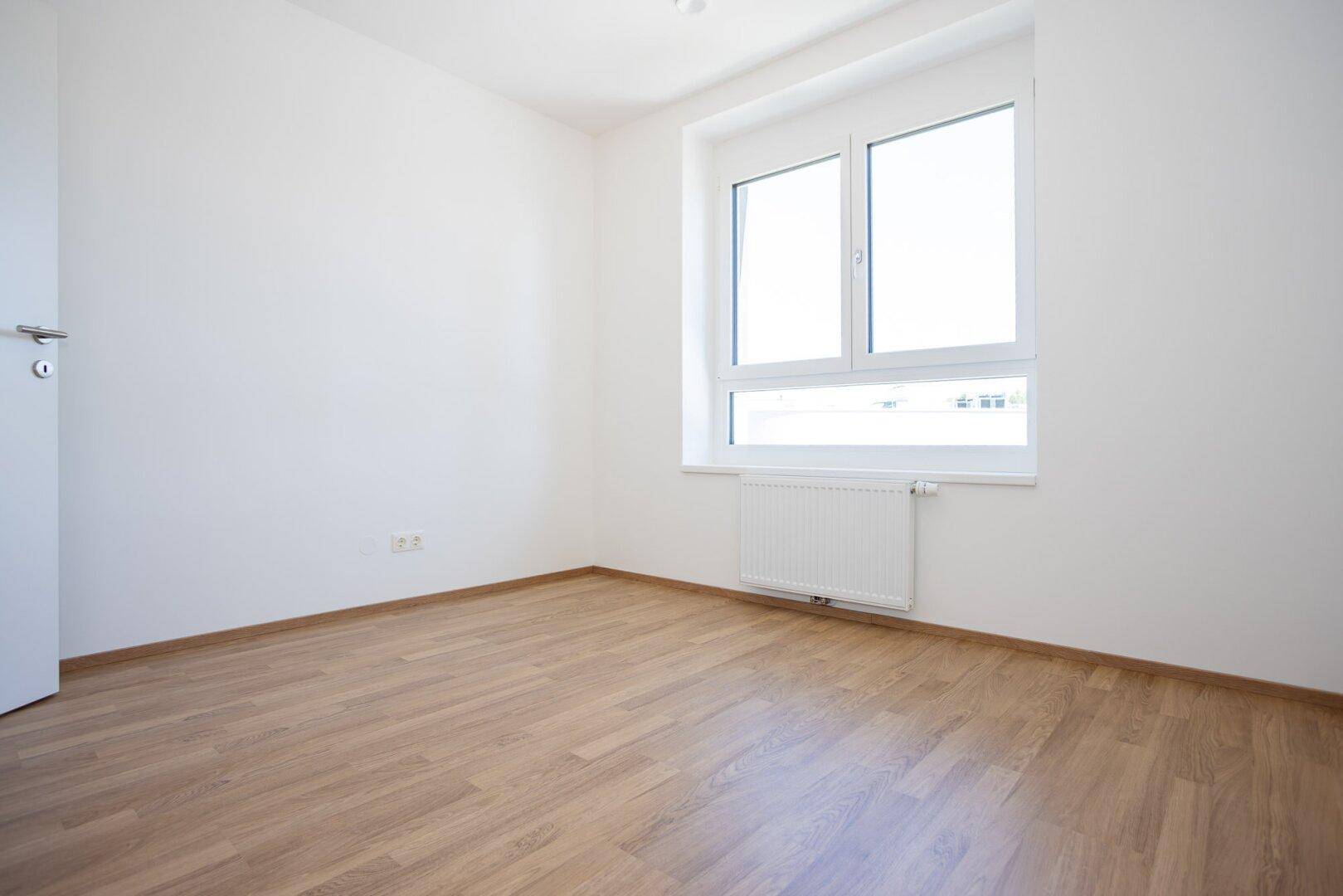 Modernes Schlafzimmer mit hellem Laminatboden und weißen Wänden, ideal für eine ruhige Wohnatmosphäre.