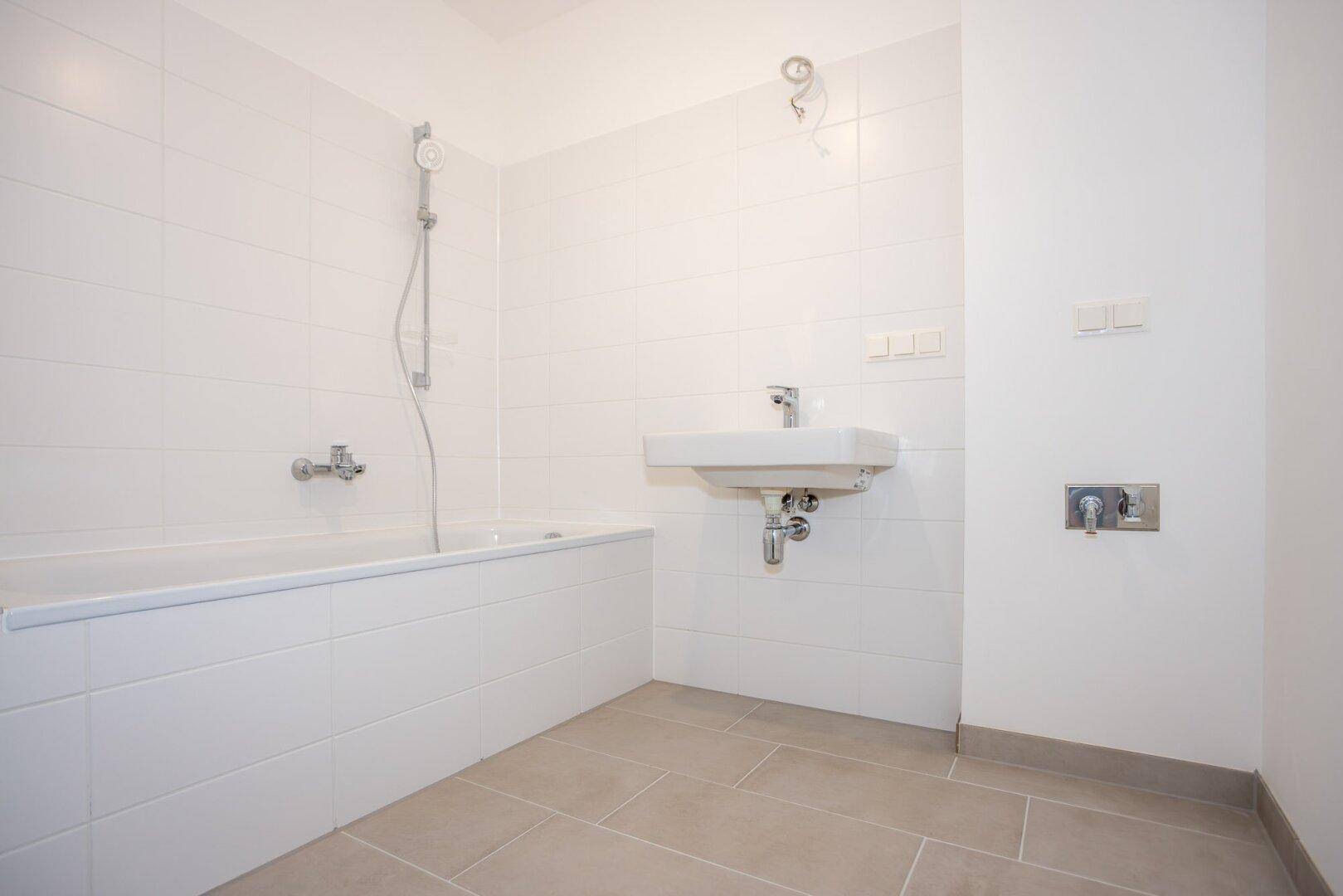 Modernes Badezimmer mit Badewanne, Waschbecken und hellen Fliesen an Wänden und Boden.