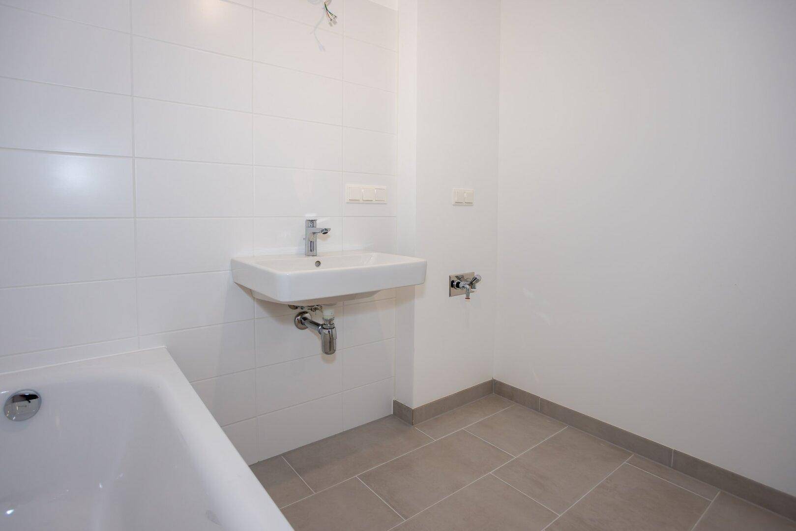 Helles Badezimmer mit Badewanne und modernem Waschbecken, ausgestattet mit weißen Fliesen.