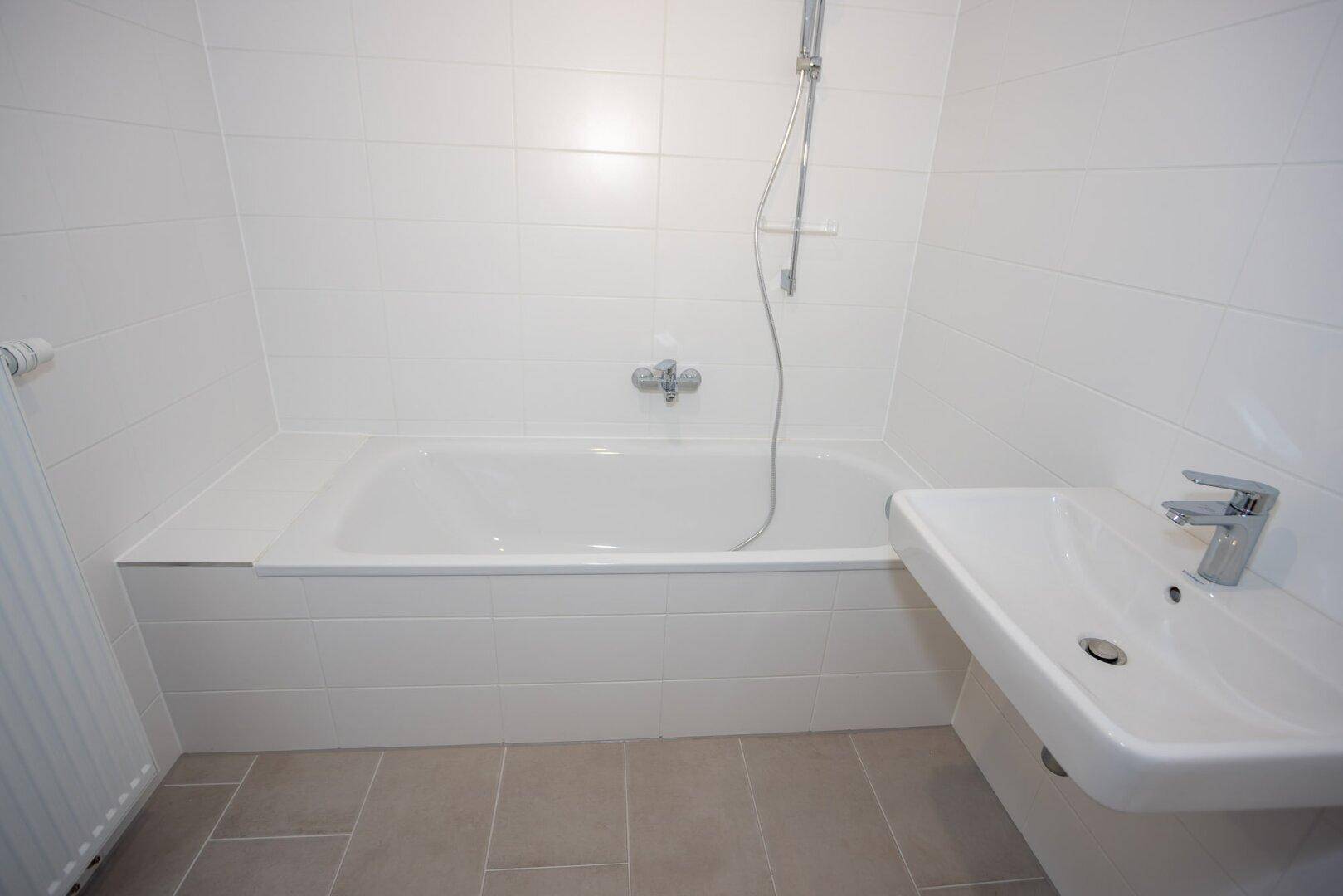 Funktionales Badezimmer mit Badewanne und Duscharmatur, sowie einem modernen Waschbecken.