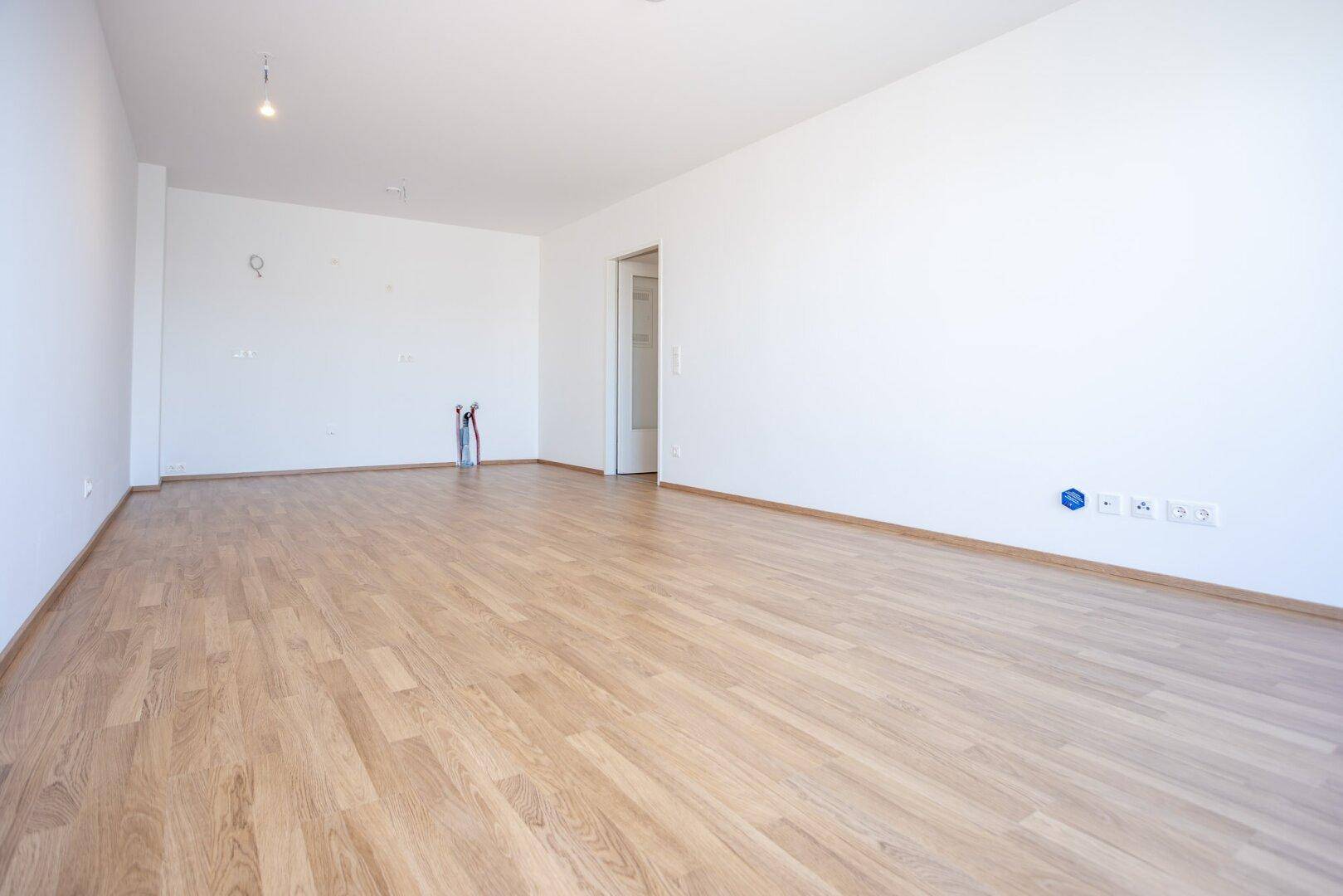 Leerer Raum mit Laminatboden und weißen Wänden, bereit für die individuelle Gestaltung.
