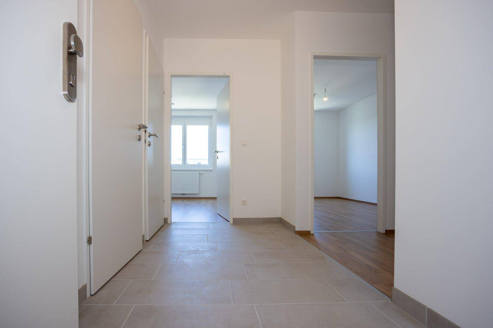 Heller Eingangsbereich mit Fliesenboden, der zu verschiedenen Zimmern der Wohnung führt.