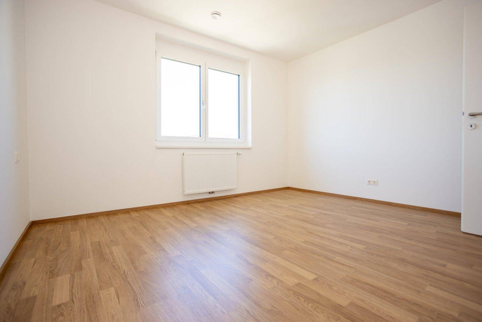 Geräumiges Schlafzimmer mit Laminatboden und Fenster, bereit für die Einrichtung.