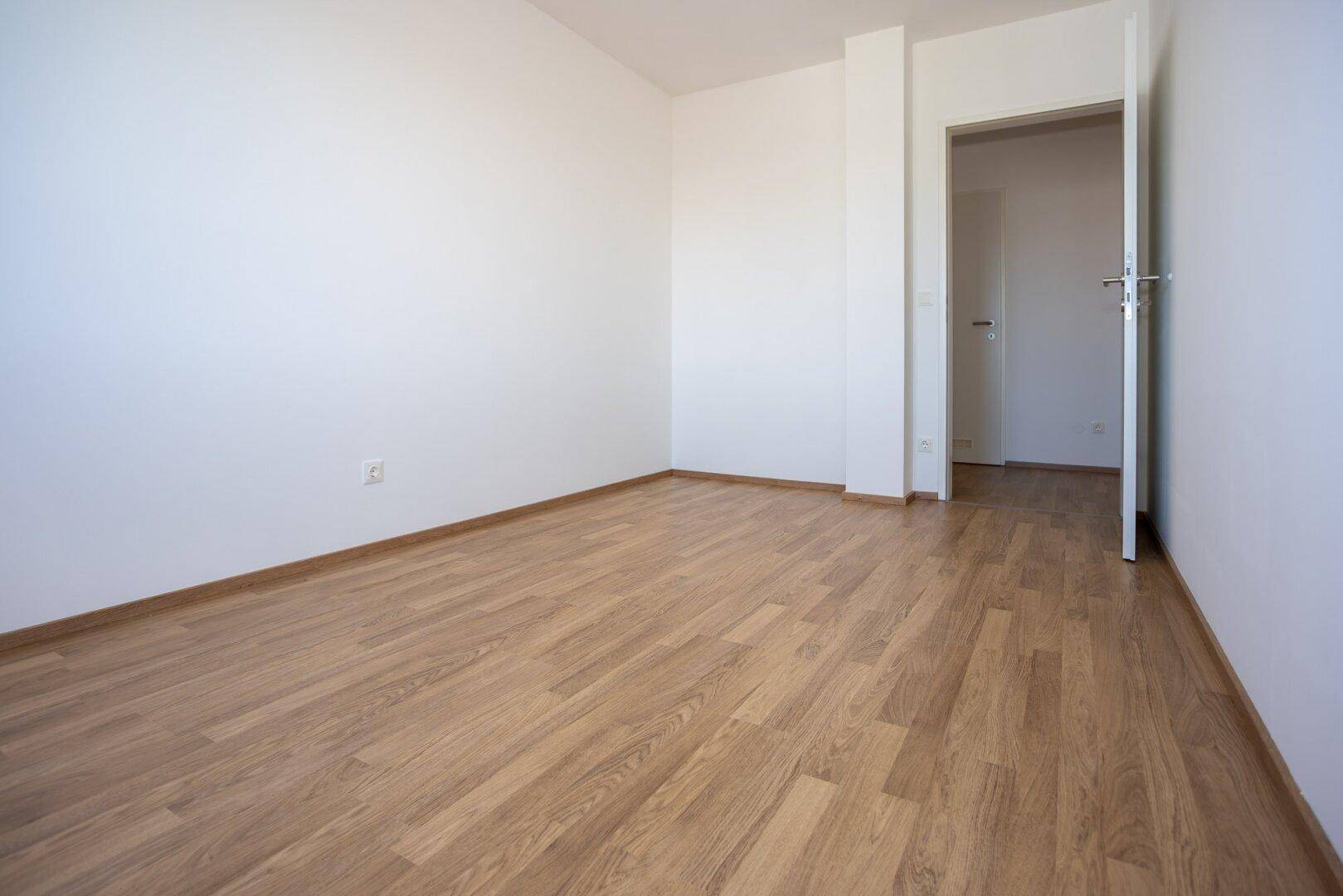 Unmöbliertes Zimmer mit Laminatboden und offener Tür, bietet vielseitige Nutzungsmöglichkeiten.