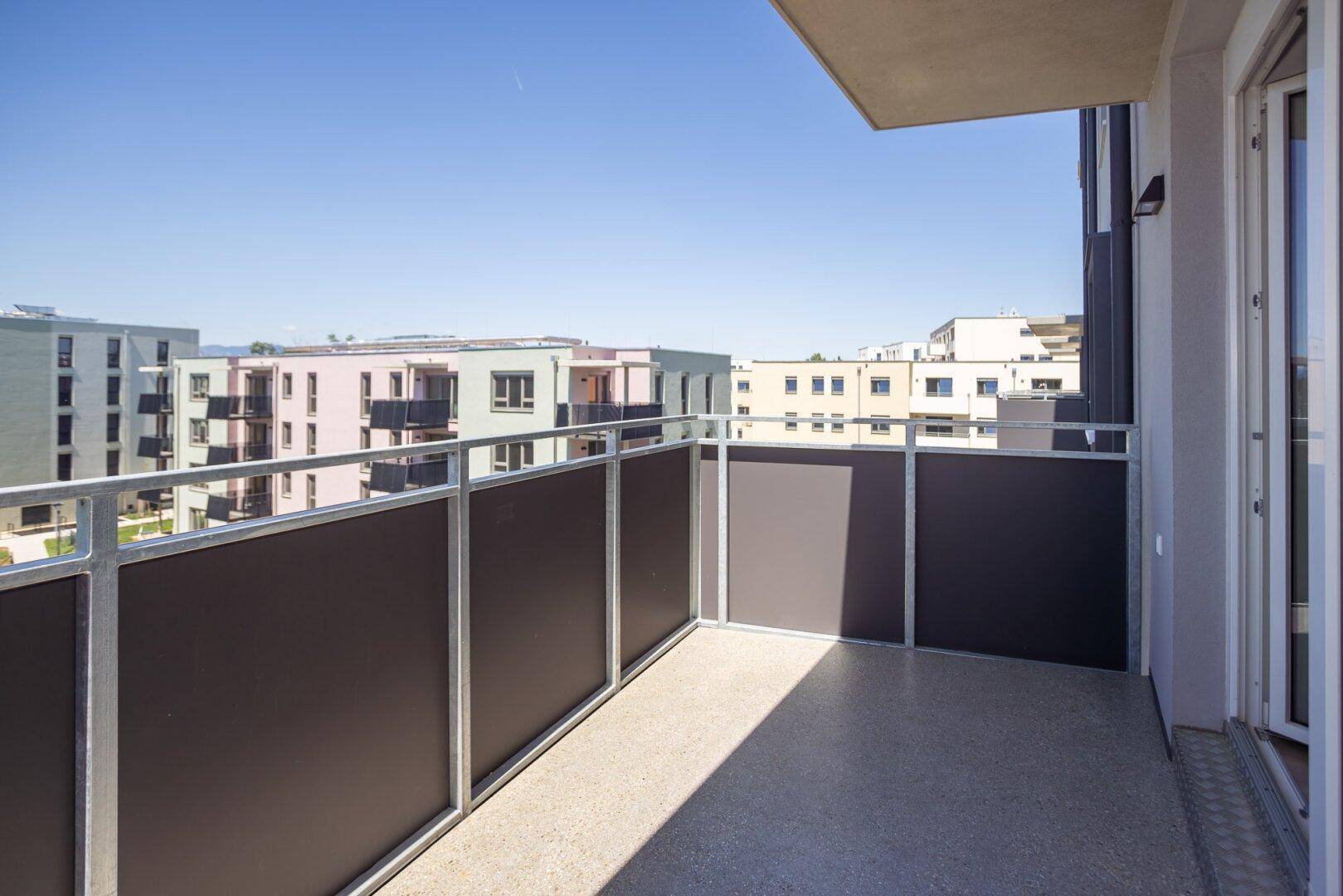 Geräumiger Balkon mit Blick auf moderne Wohngebäude und viel Sonnenlicht.
