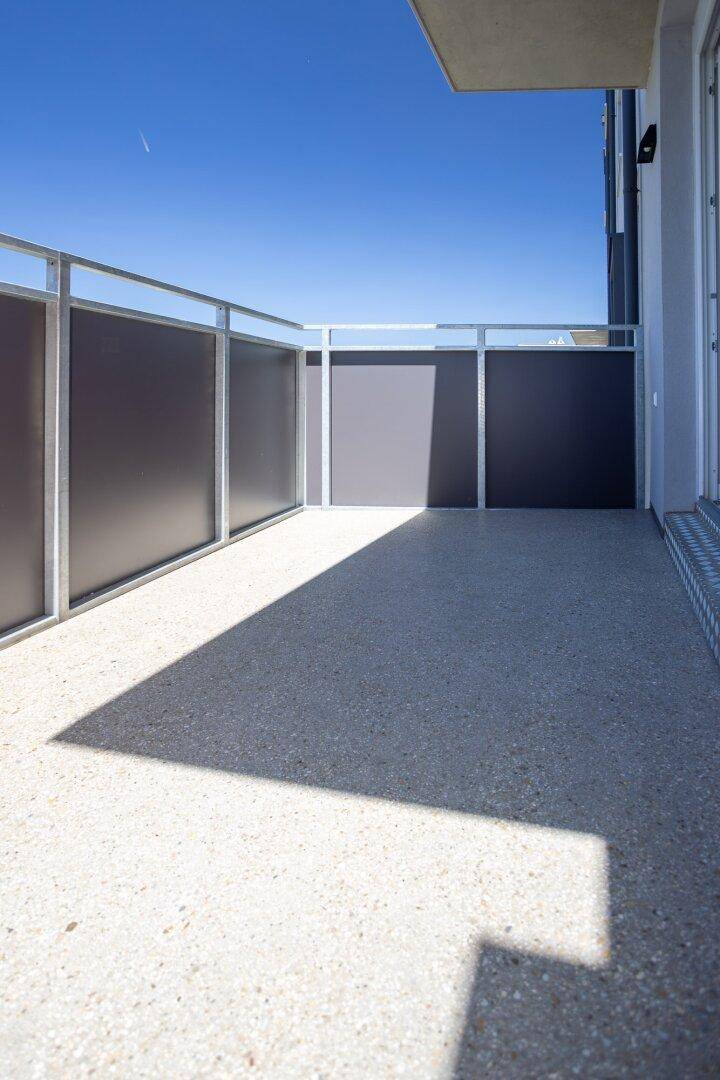 Geräumiger Balkon mit modernem Geländer und sonnigem Bodenbelag, ideal zum Entspannen.