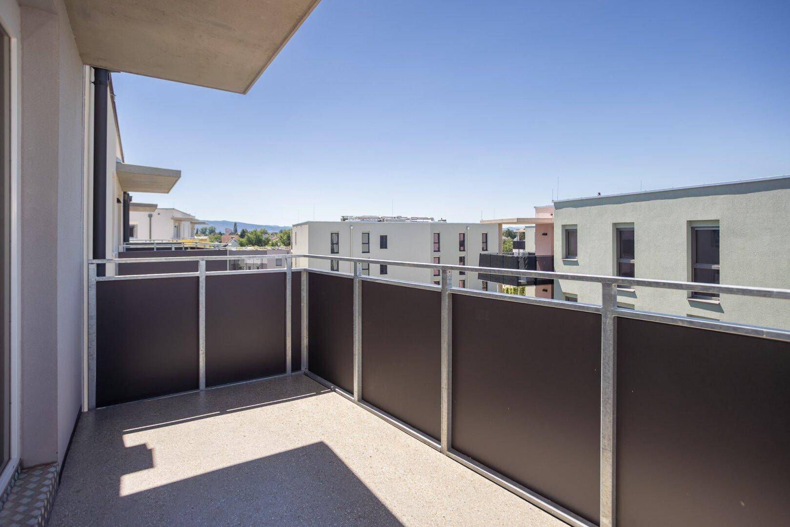 Sonniger Balkon mit modernem Geländer und Ausblick auf die Stadt und die umliegende Landschaft.