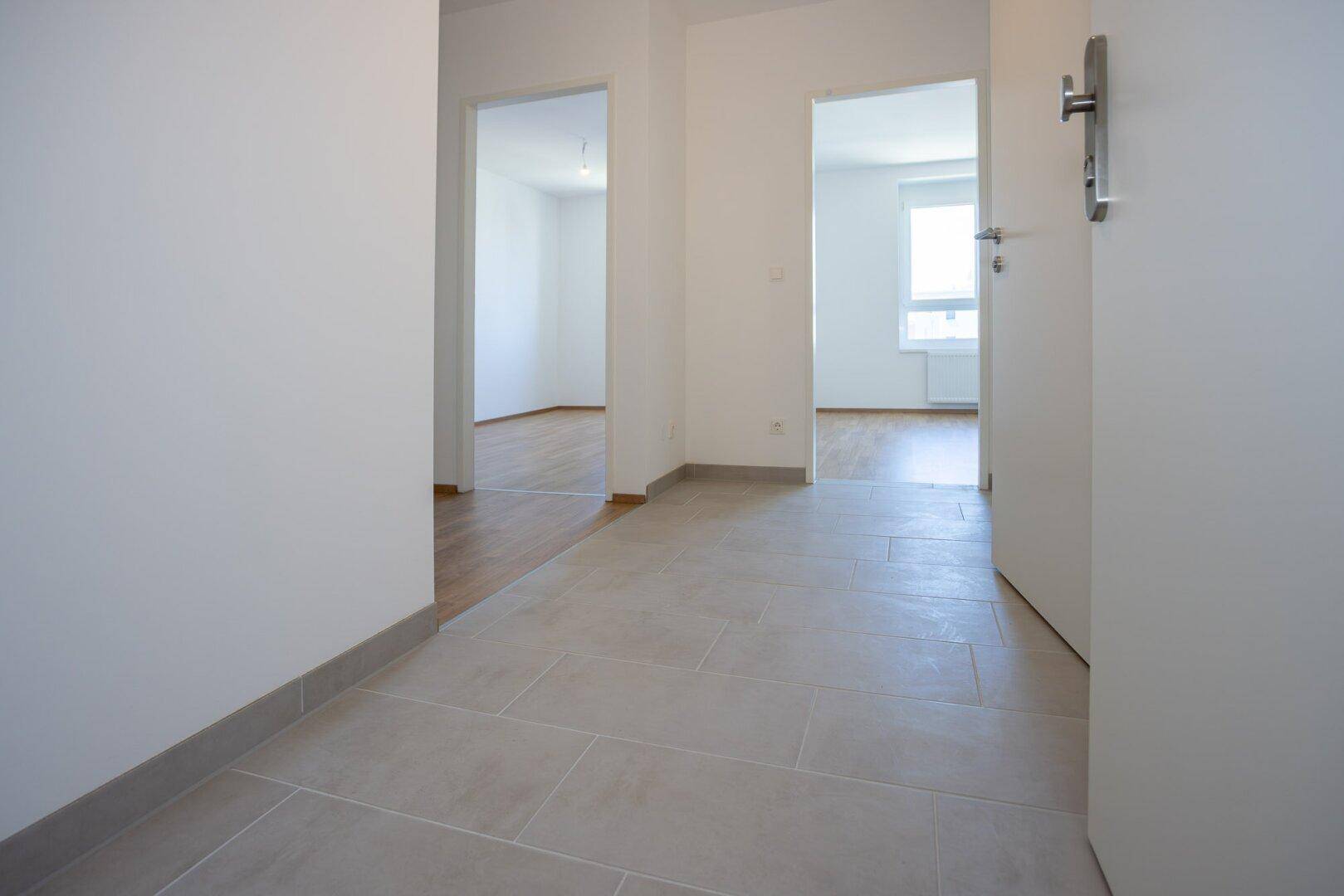 Heller Eingangsbereich mit Fliesenboden, der zu verschiedenen Zimmern der Wohnung führt.