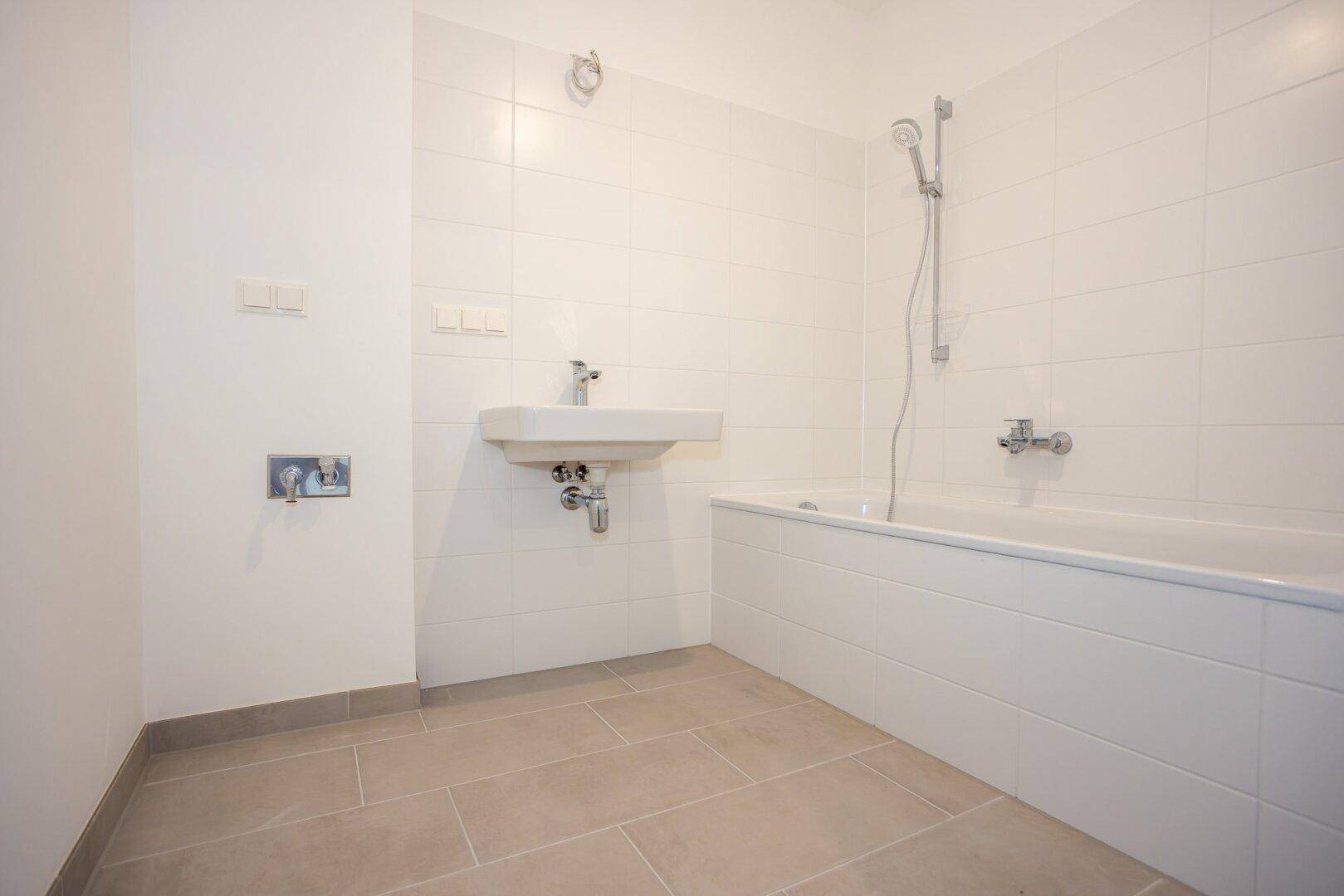Helles Badezimmer mit Waschbecken und Badewanne inklusive Duschfunktion, sauber gefliest.