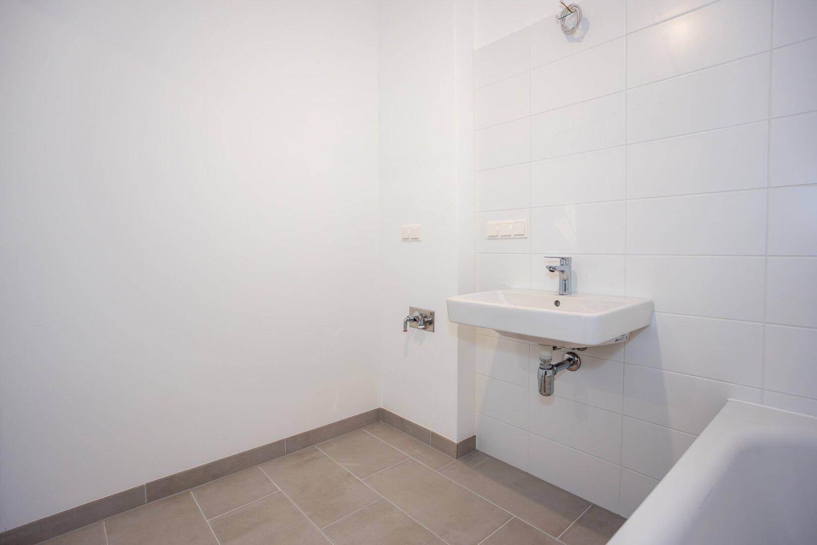 Modernes Badezimmer mit Waschbecken und Badewanne, hell gefliest und funktional gestaltet.