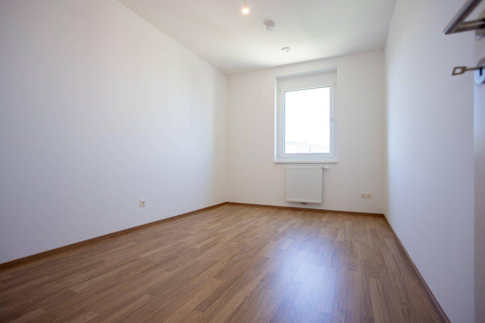 Kleineres Schlafzimmer mit Laminatboden und einem einzelnen Fenster, ideal als Kinder- oder Gästezimmer.