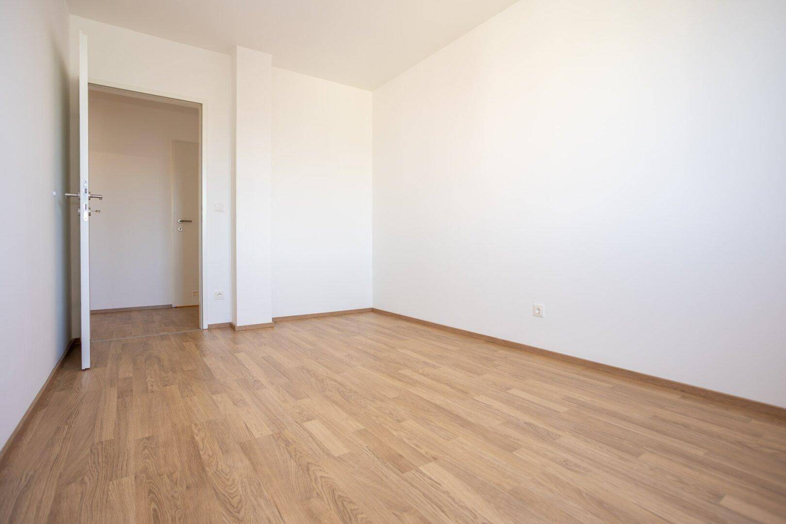 Leeres Zimmer mit Laminatboden und weiß gestrichenen Wänden, bereit zur Einrichtung.