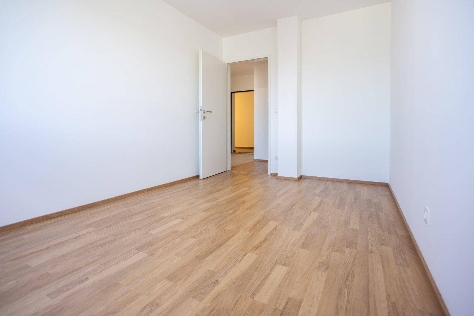 Helles Zimmer mit Laminatboden und offener Tür zu einem weiteren Bereich der Wohnung.