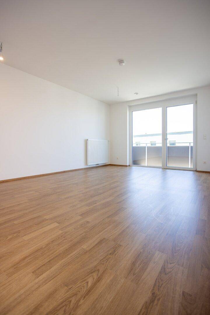 Großes, helles Wohnzimmer mit Laminatboden und Zugang zum Balkon, bietet viel Gestaltungsfreiheit.