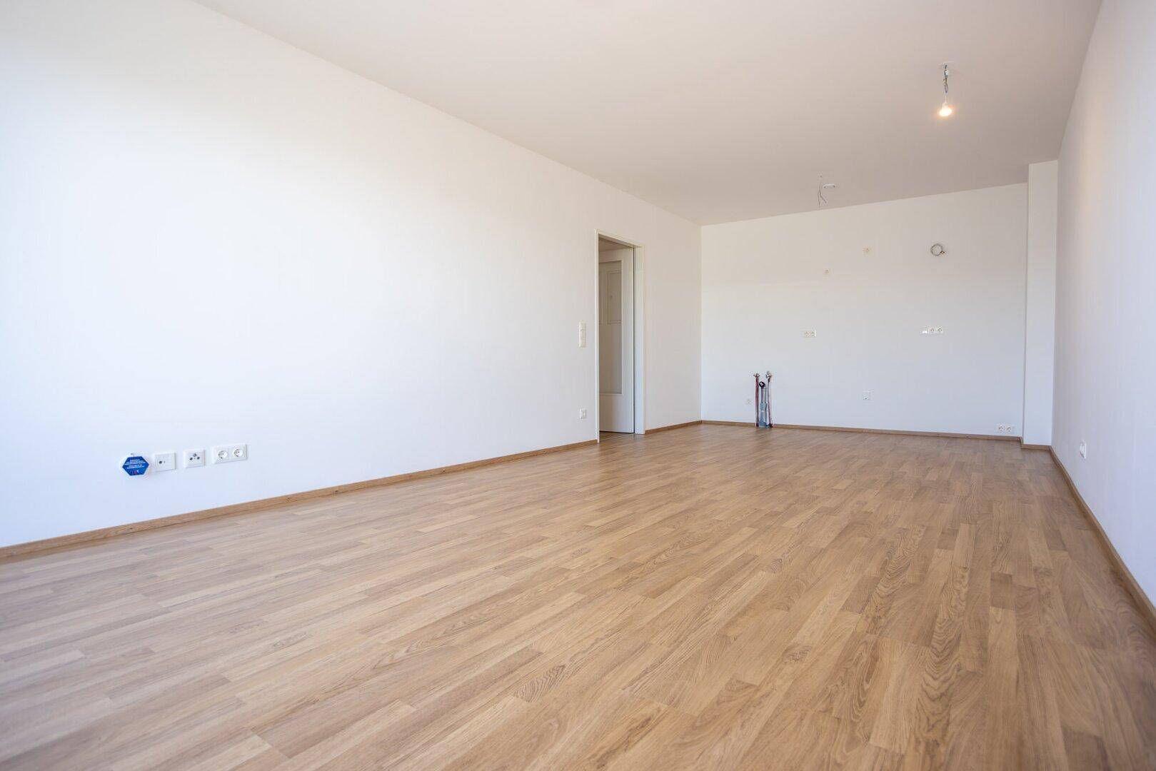 Geräumiges Wohnzimmer mit Laminatboden und weißen Wänden, bereit für die Installation von Medien.