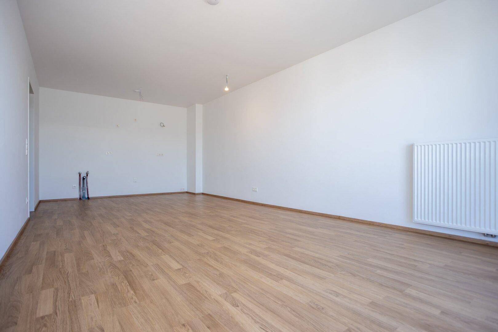Großzügiges Wohnzimmer mit Laminatboden und Heizkörper, bietet viel Platz für Möbel.