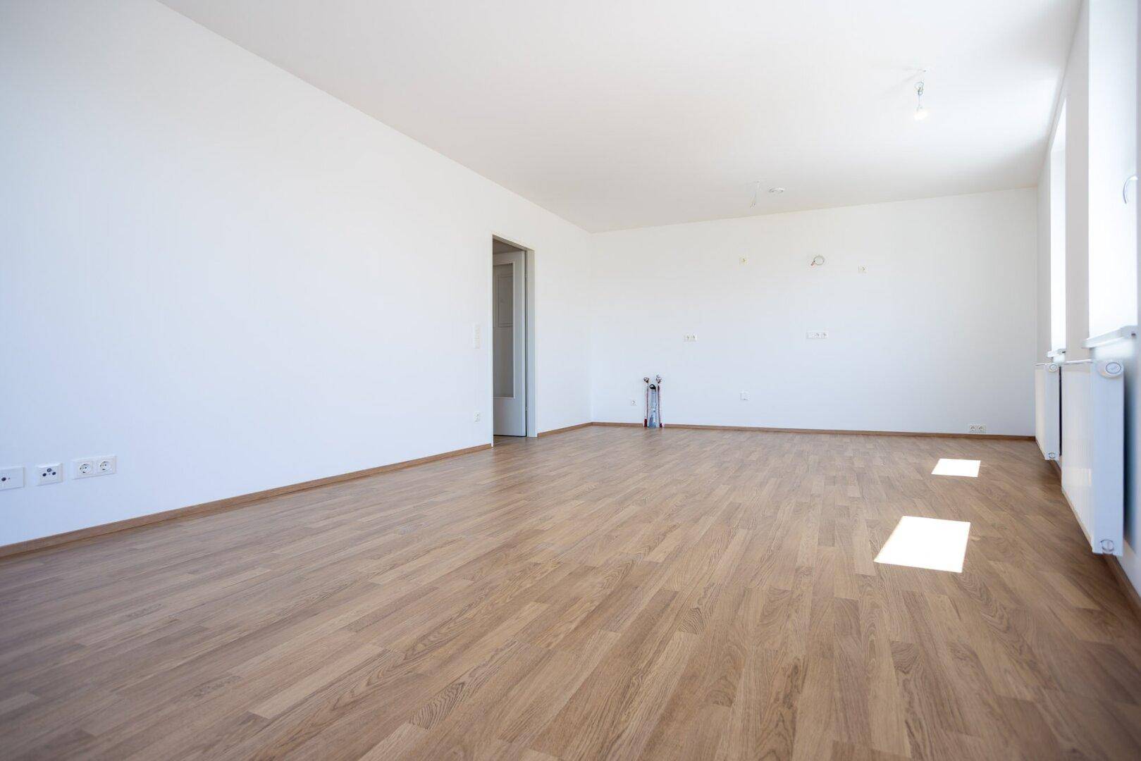 Geräumiger, heller Raum mit Laminatboden und weißen Wänden, vorbereitet für eine Küche.