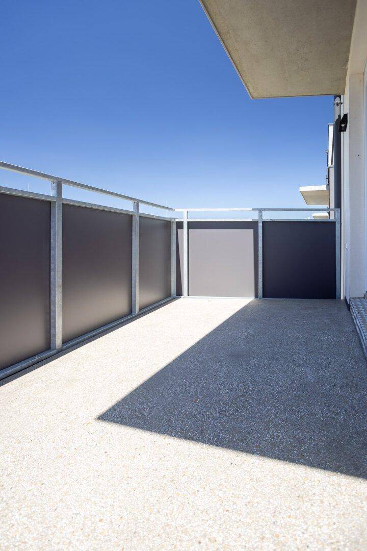 Sonniger Außenbereich mit Betonboden und moderner Metallbrüstung unter blauem Himmel.